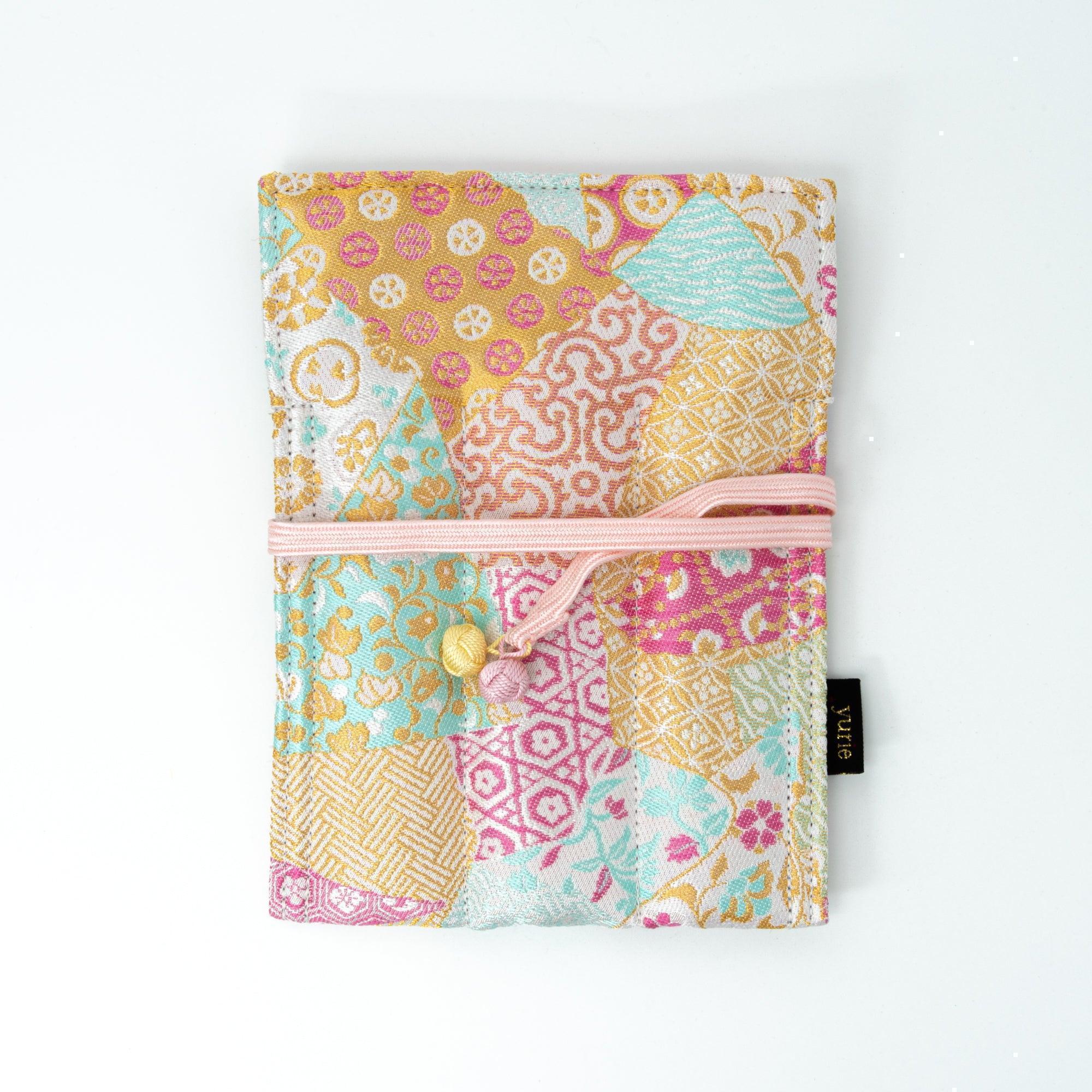 A pastel-colored Japanese fountain pen case made of Nishijin silk, featuring floral and geometric patterns, tied with a pink cord, on a white background.
