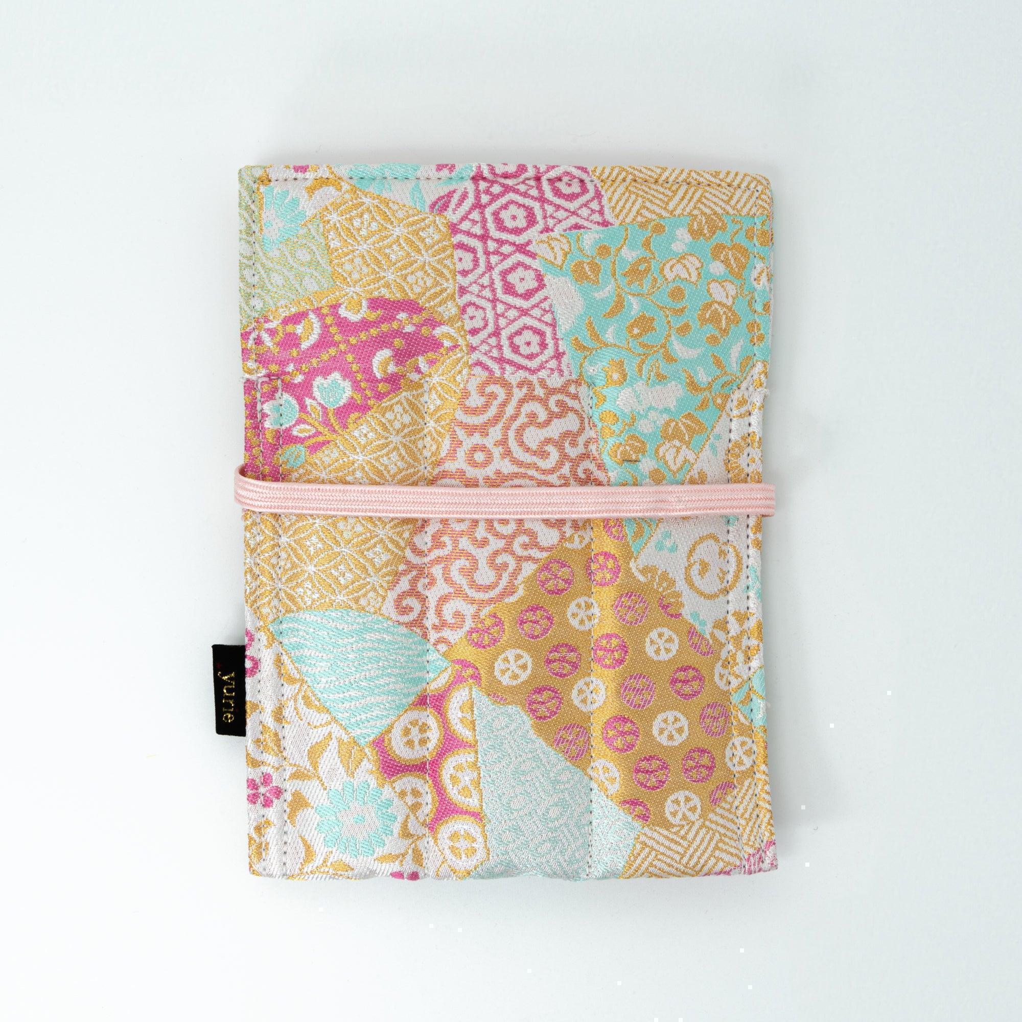 A pastel-colored Japanese fountain pen case of Nishijin silk with floral and geometric designs, tied with a pink cord, placed on a white surface.