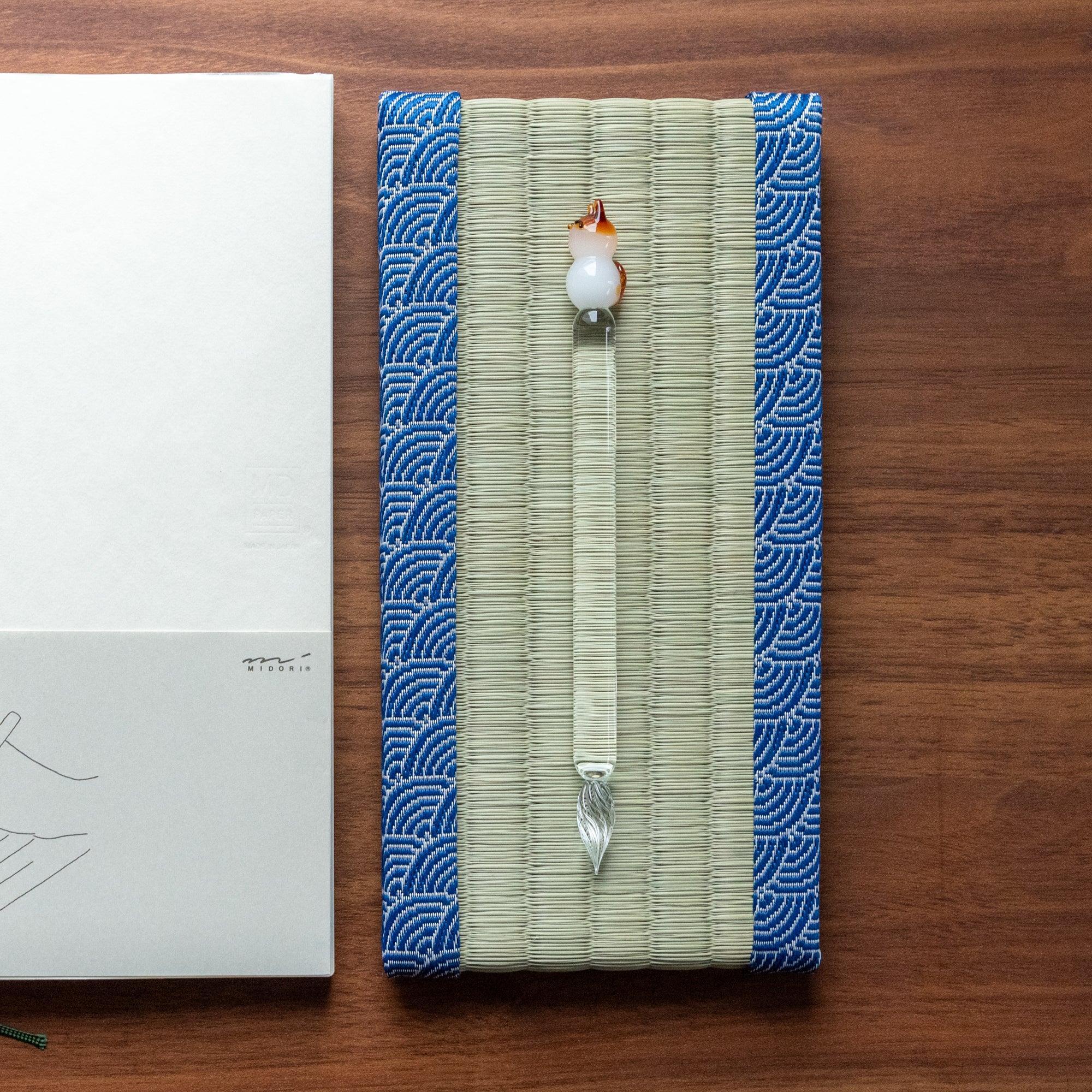 Glass pen with a fox design on a tatami pen tray featuring traditional blue wave patterns, highlighting a unique piece of handcrafted Japanese stationery.