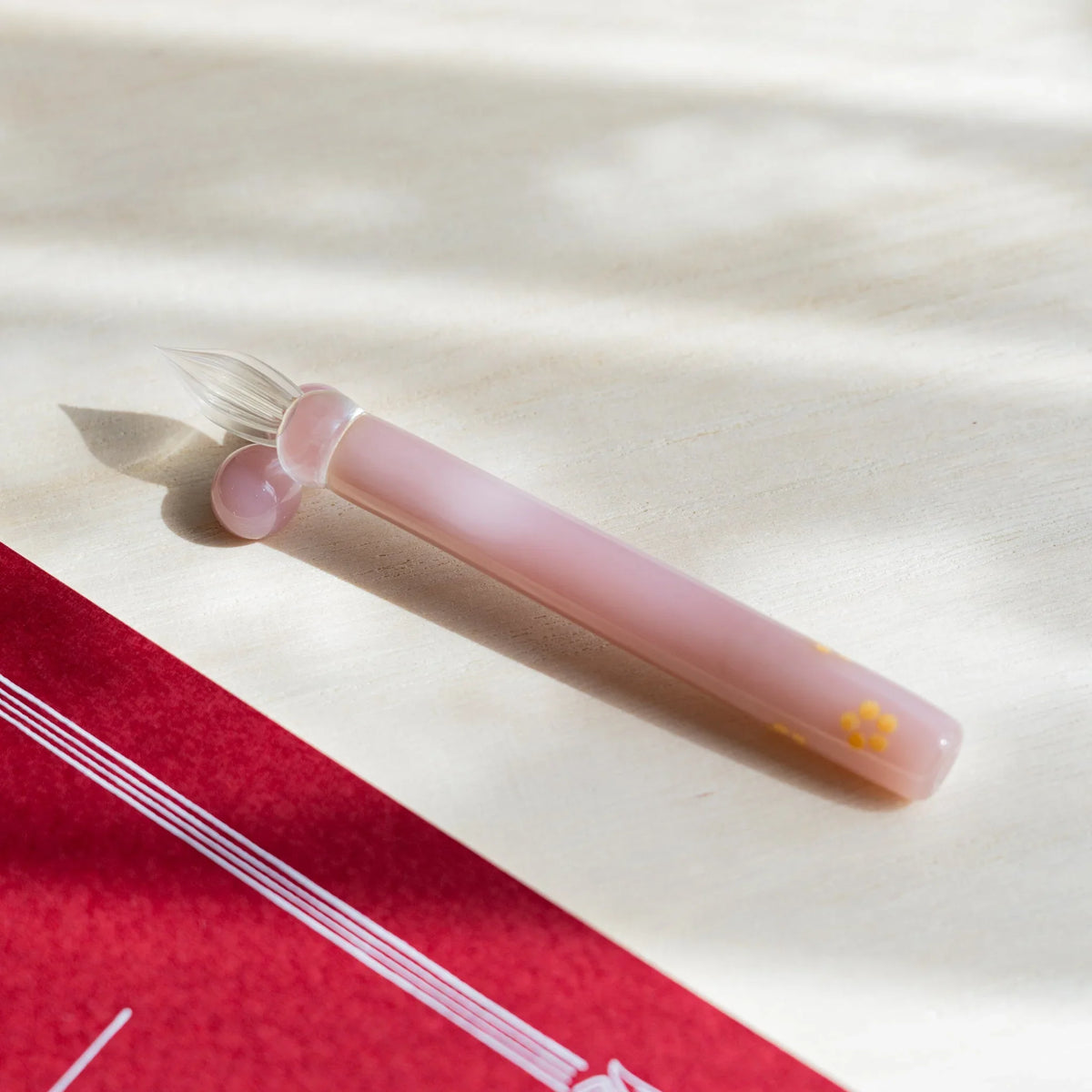 Blush Pink Flowers glass dip pen laid on pale wood, pink barrel with a yellow blossom near the end