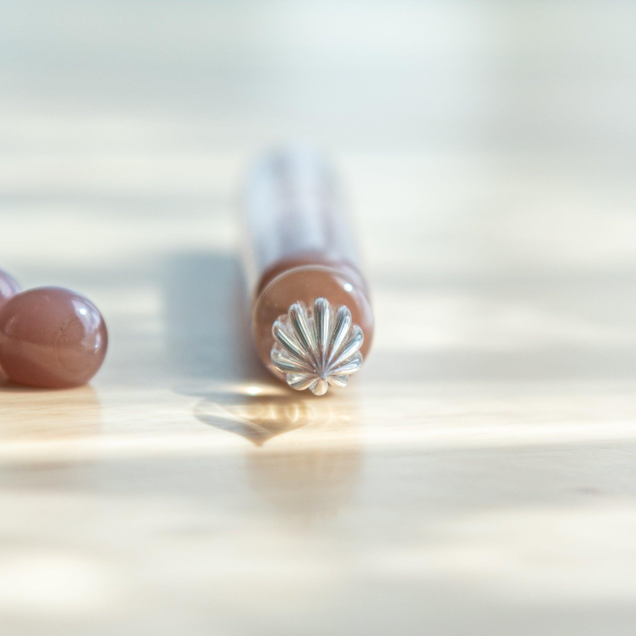 Front view of a Japanese pink glass dip pen with a twisted clear nib and glossy body, casting a soft shadow on the wooden desk.