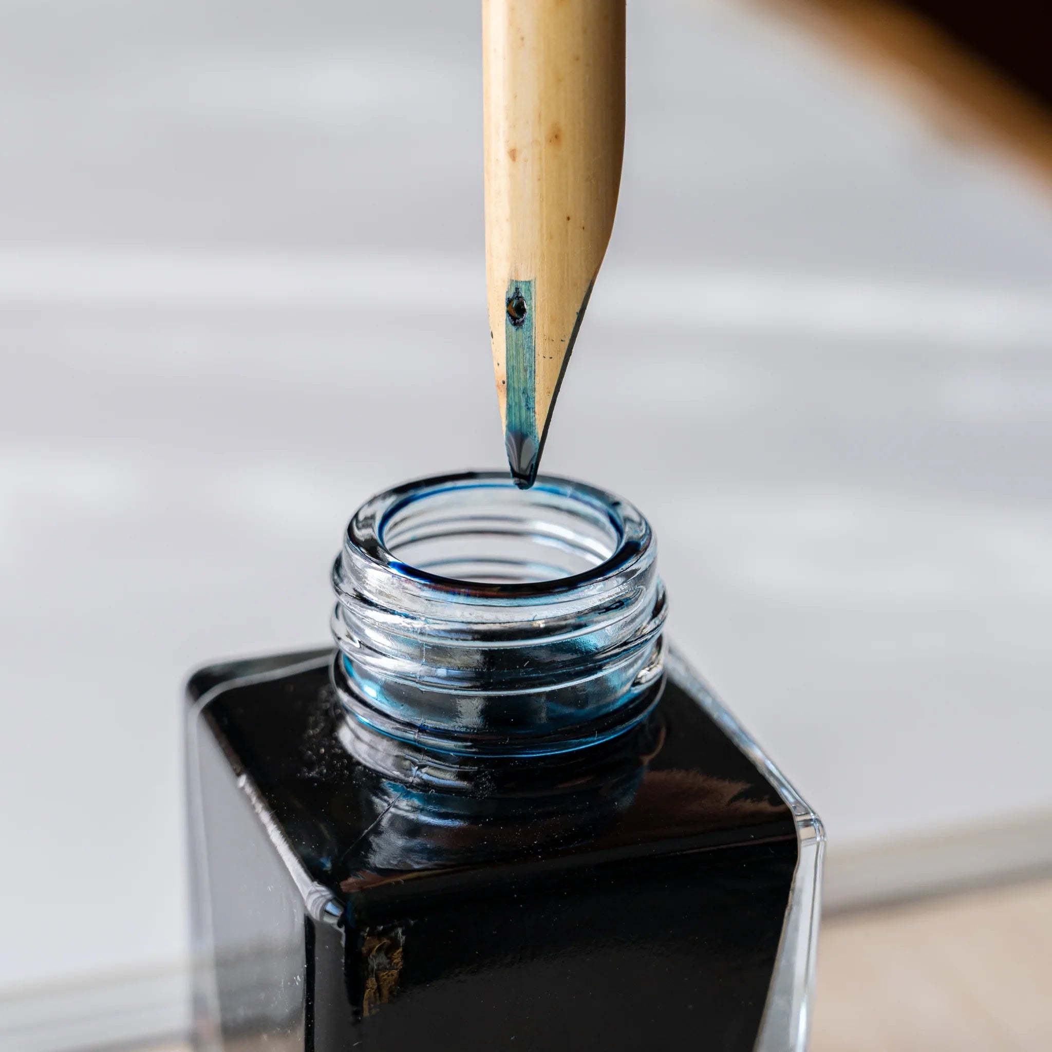 Boku-Undo bamboo pen nib with blue-black ink hovering just above open glass ink bottle, dark ink inside