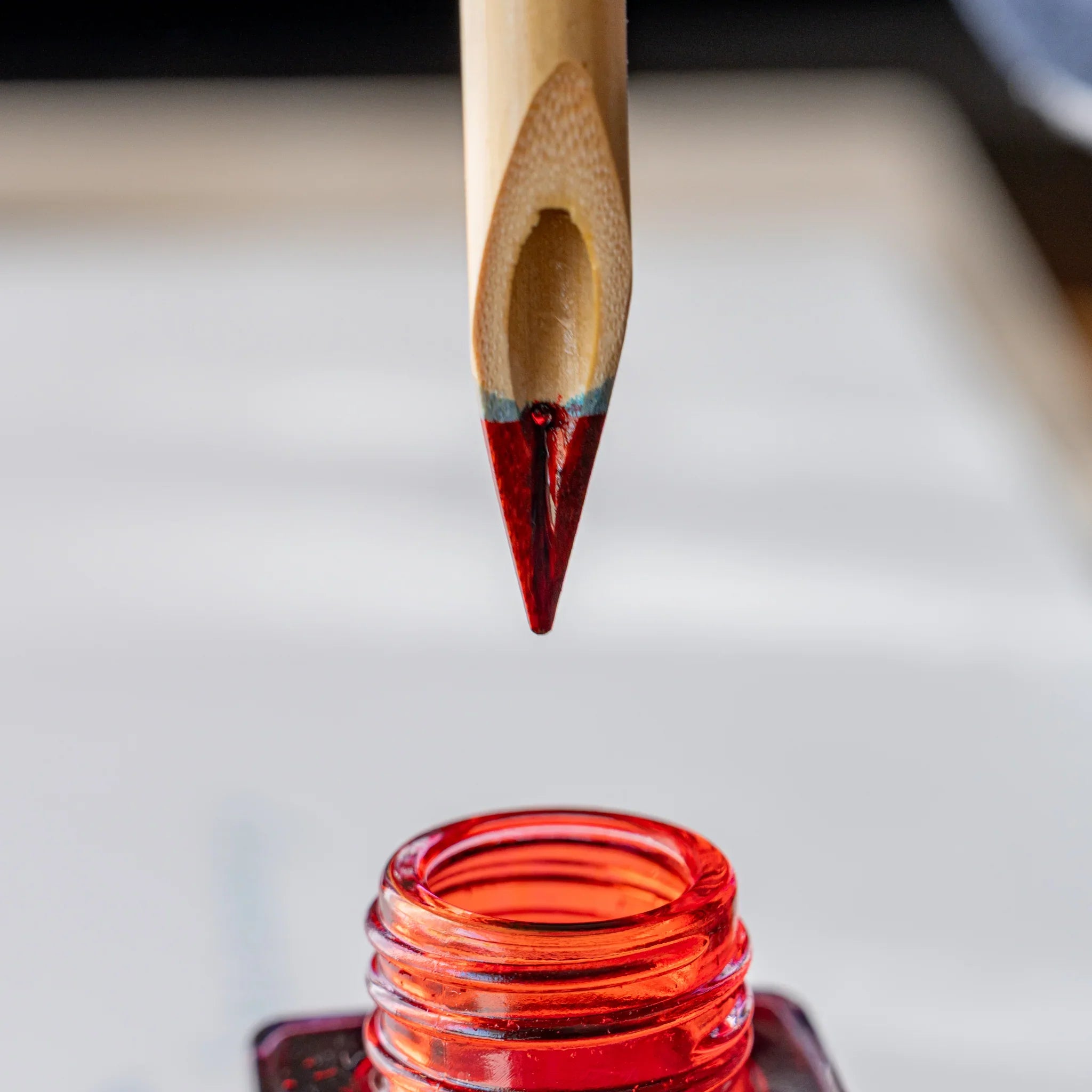 Boku-Undo bamboo dip pen nib lifted above open red ink bottle with red ink coating the tip