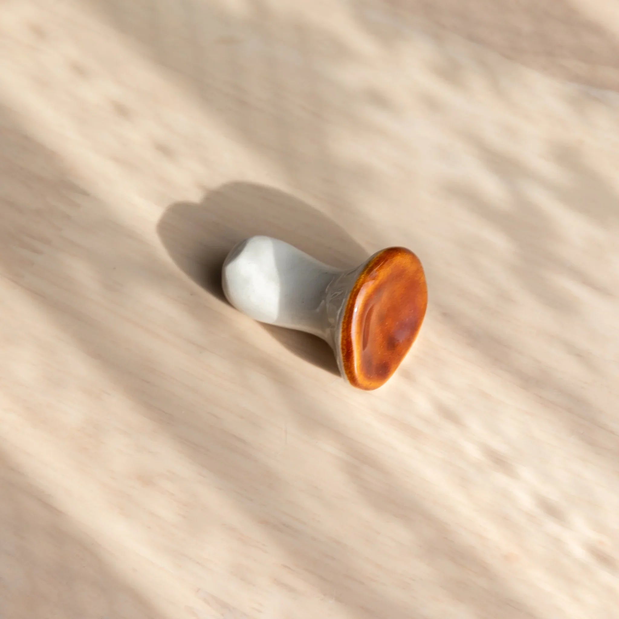 Brown mushroom-shaped handcrafted ceramic pen rest with contrasting white stem, overhead angle view lighting detail