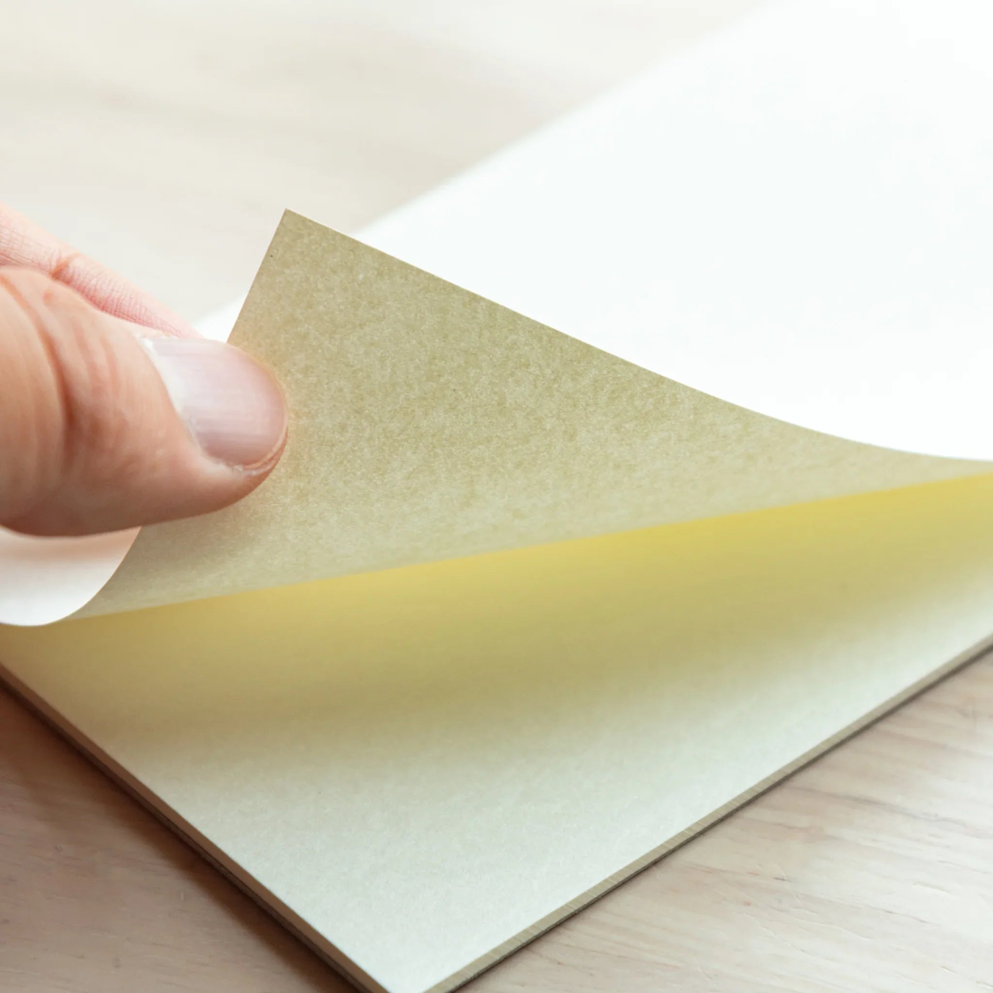 Hand peeling a page from Bullet Jotter writing pad, showing bright white Soliste paper and yellow glue spine