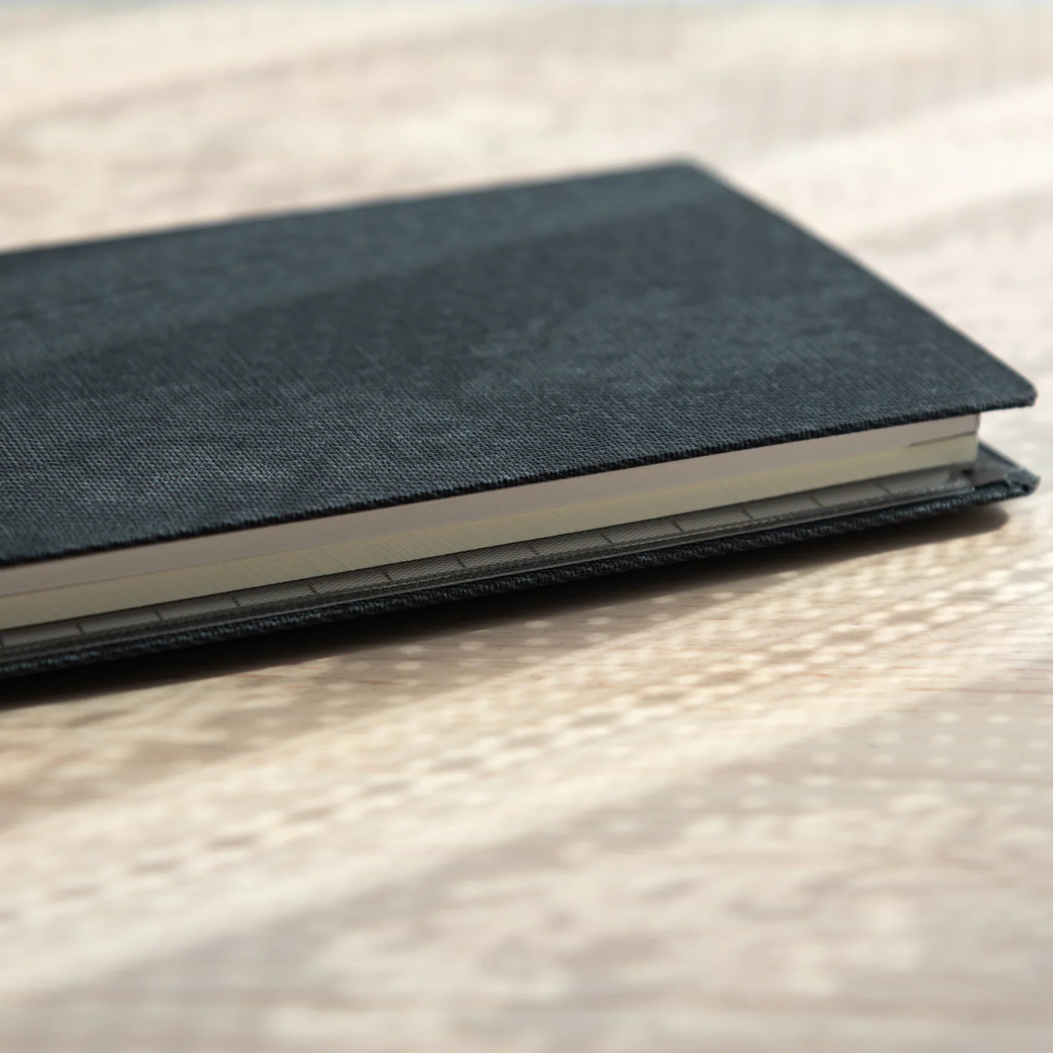 Angled side view of closed Bullet Jotter black gabardine cover on textured surface, sheet edges visible between covers