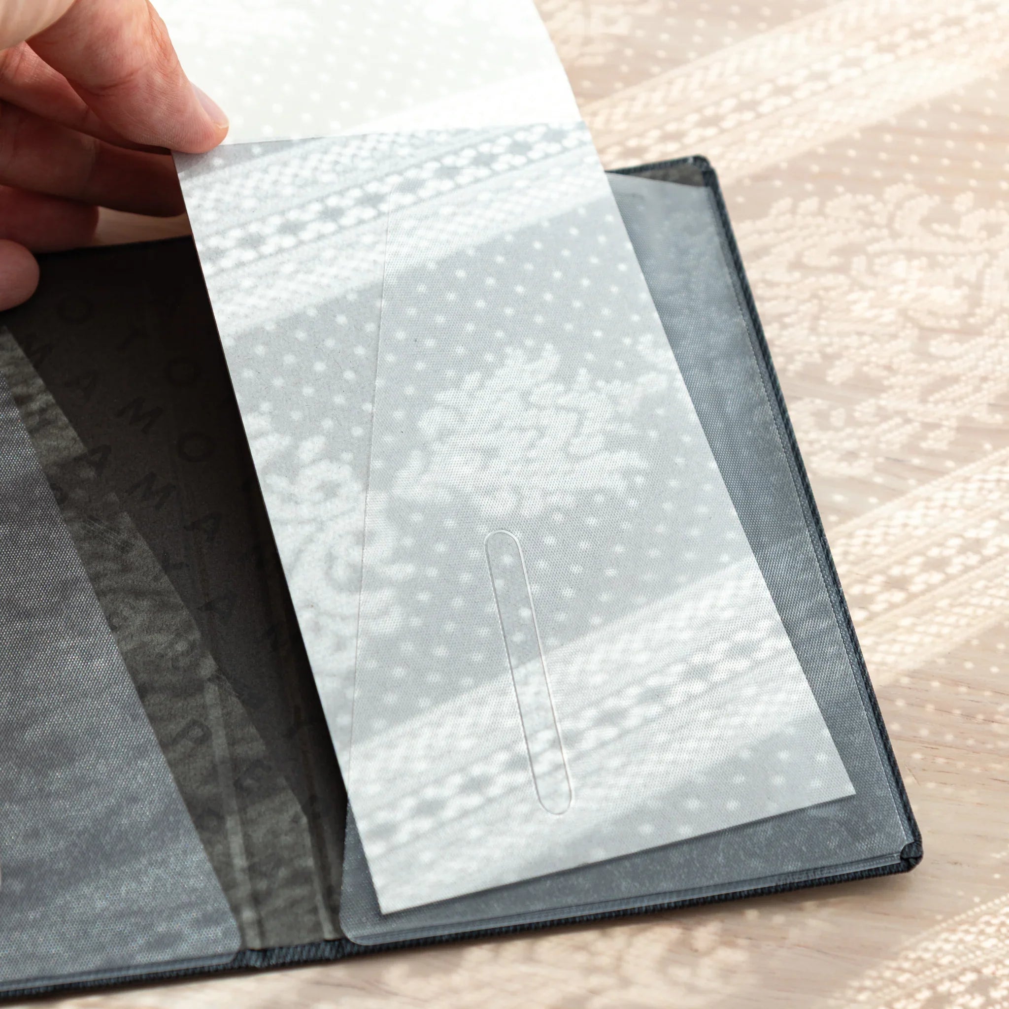 Hand holding open Bullet Jotter black gabardine cover, showing left clear pocket with slot tab and Yamamoto Paper lining