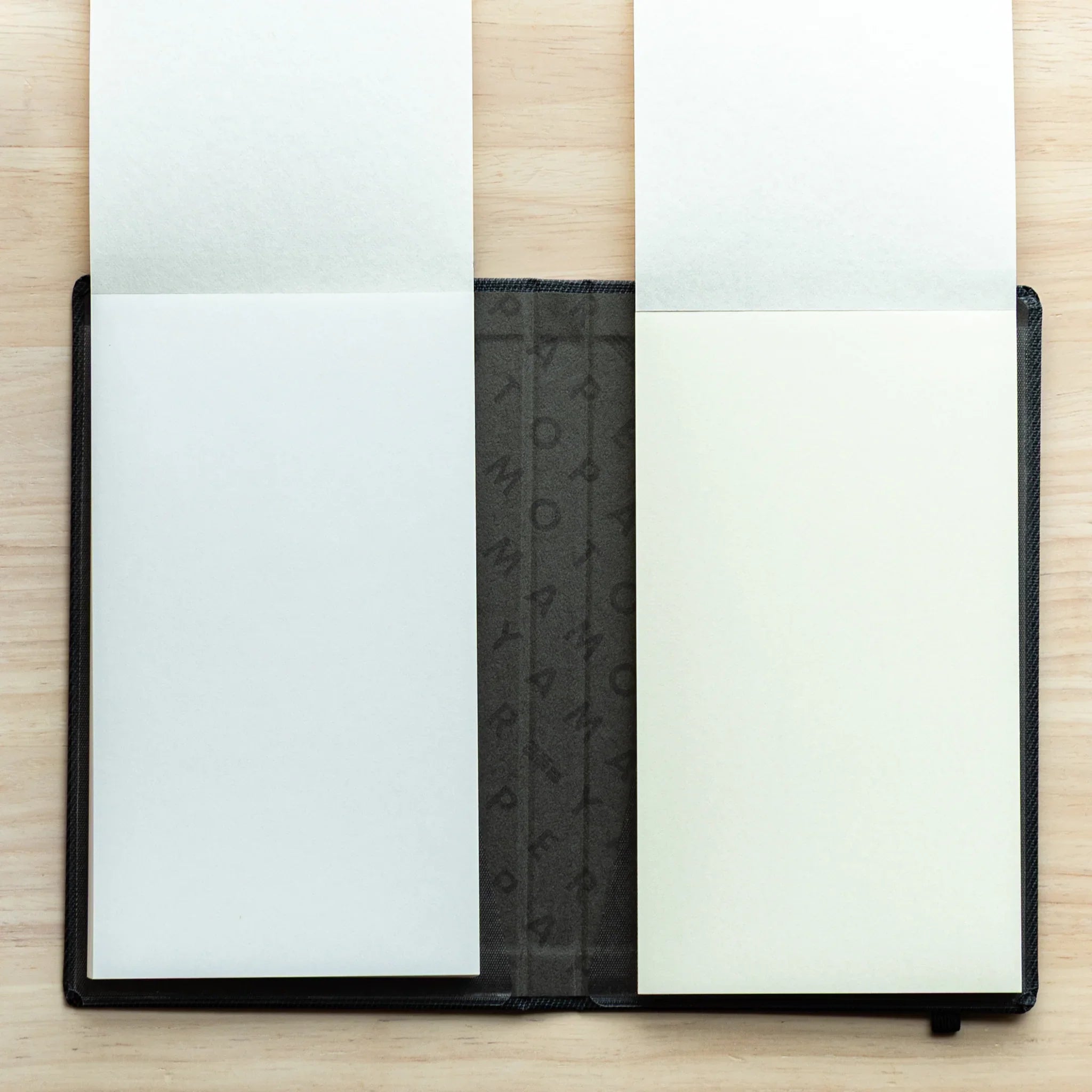 Bullet Jotter black gabardine cover open, both pads with blank pages facing up: light blue-tinted left, bright white right