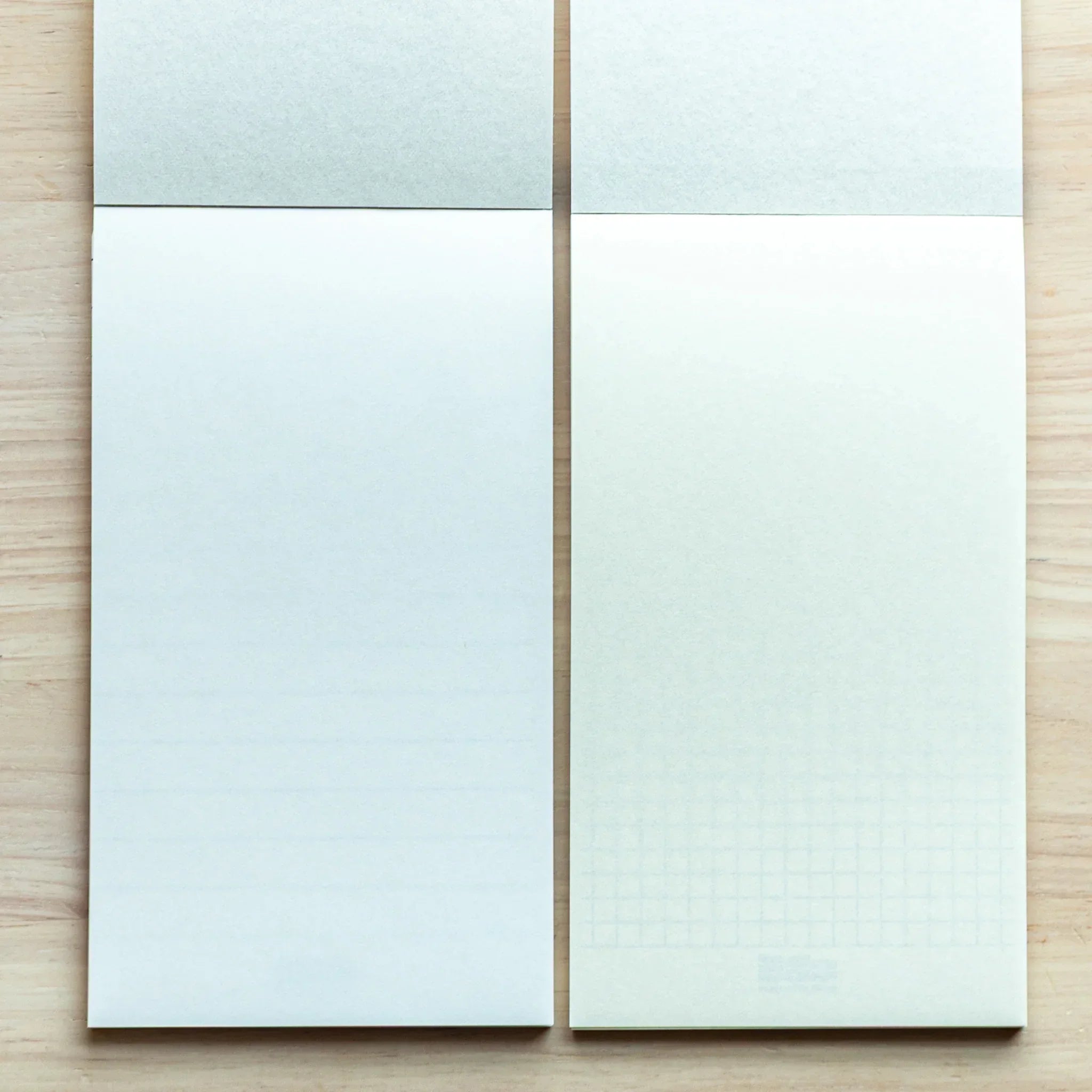 Two Bullet Jotter writing pads side by side on wood: left with light blue-tinted paper, right with bright white paper