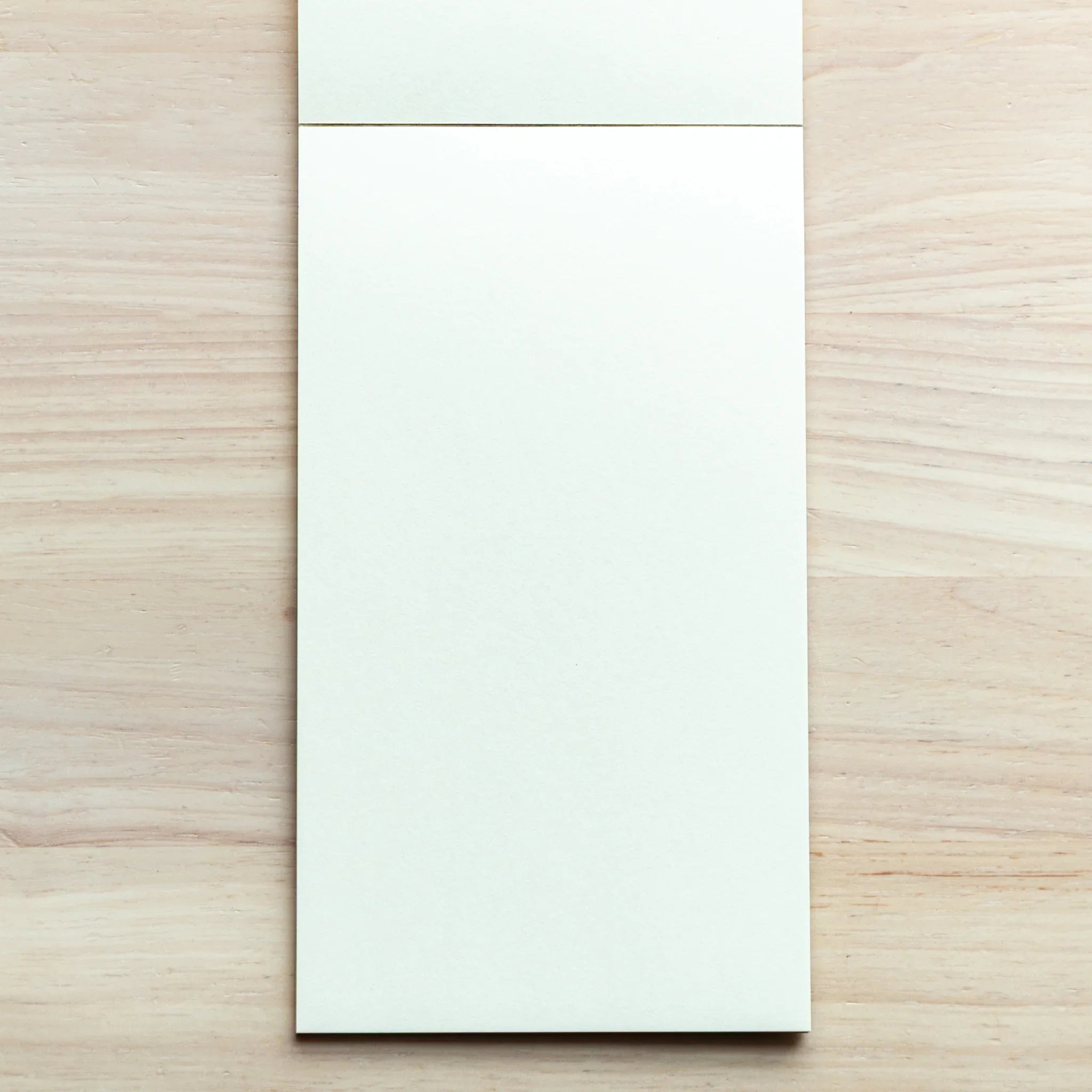 Sheep Clouds Bond writing pad on light wood, top view, thin black glue-bound spine at top, light blue-tinted blank page