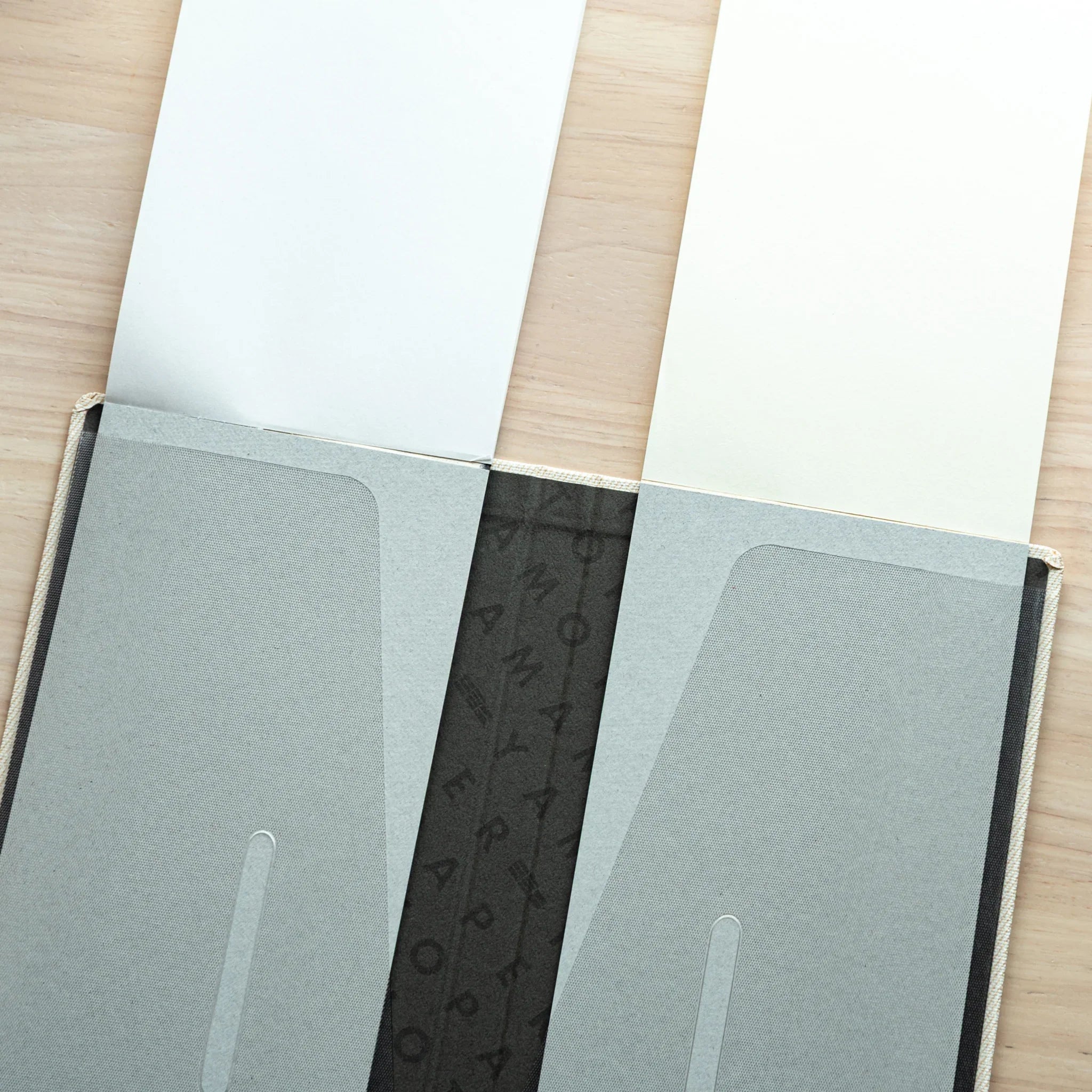 Close-up of Bullet Jotter ivory white cover interior, two clear pockets with slot tabs, pads inside, patterned spine center