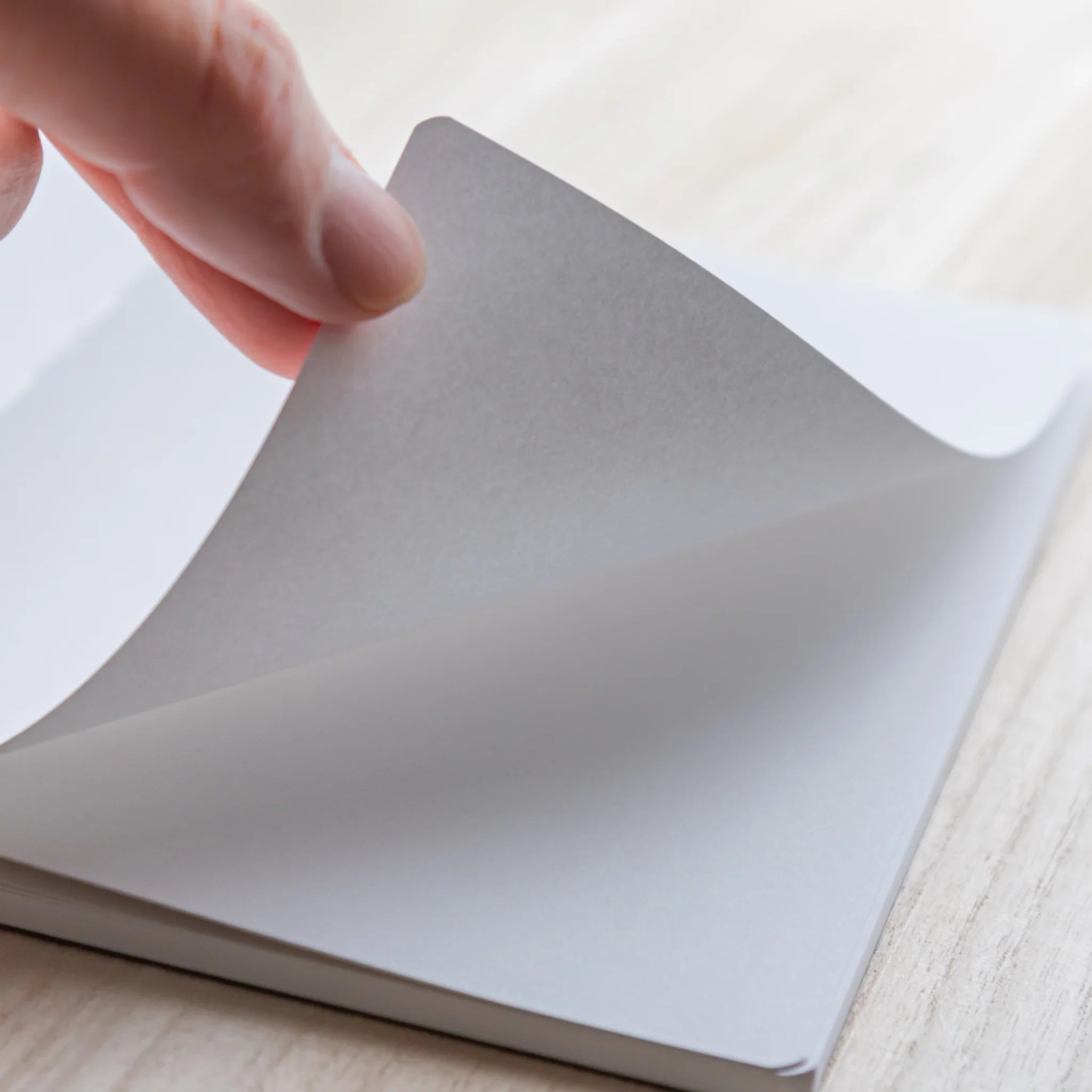 Hand lifting a blank page of Japanese Notebook, turning pages on a light wooden desk.