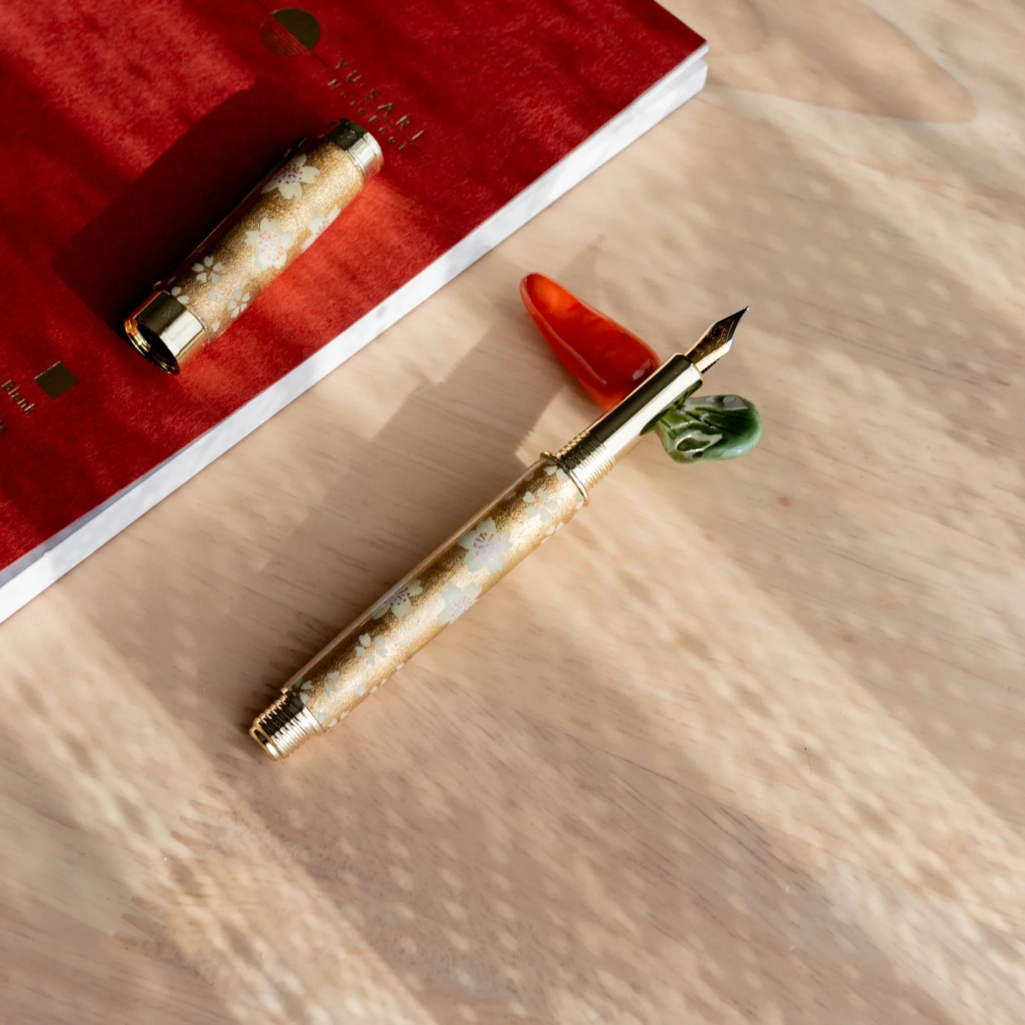 Orange carrot handcrafted pen rest with green leafy stem accent and functional groove along body shape on neutral surface