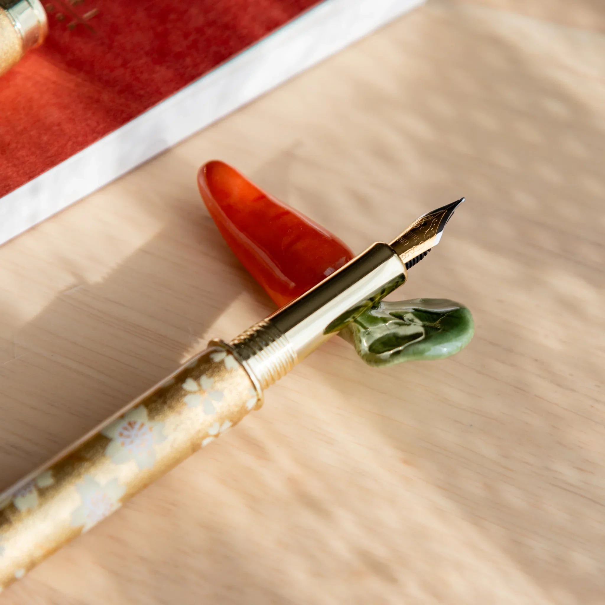 Bright orange handcrafted carrot pen rest with leafy green top detail and curved functional pen slot on neutral surface