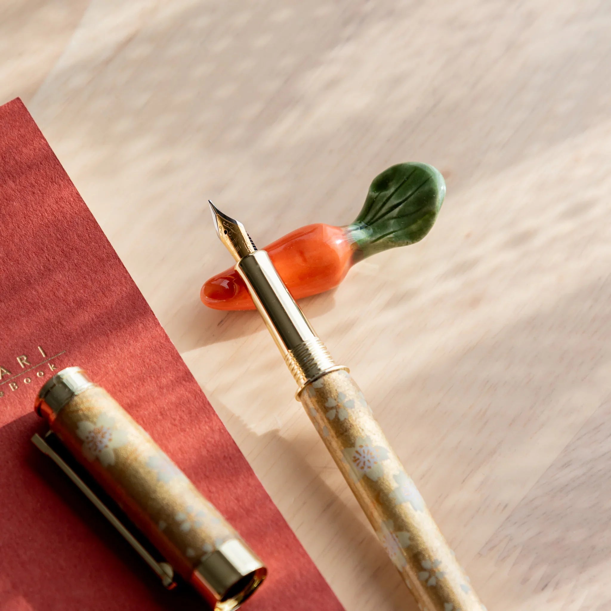 Vibrant orange carrot-shaped ceramic handcrafted pen rest featuring green leaf attachment overall shape close shot