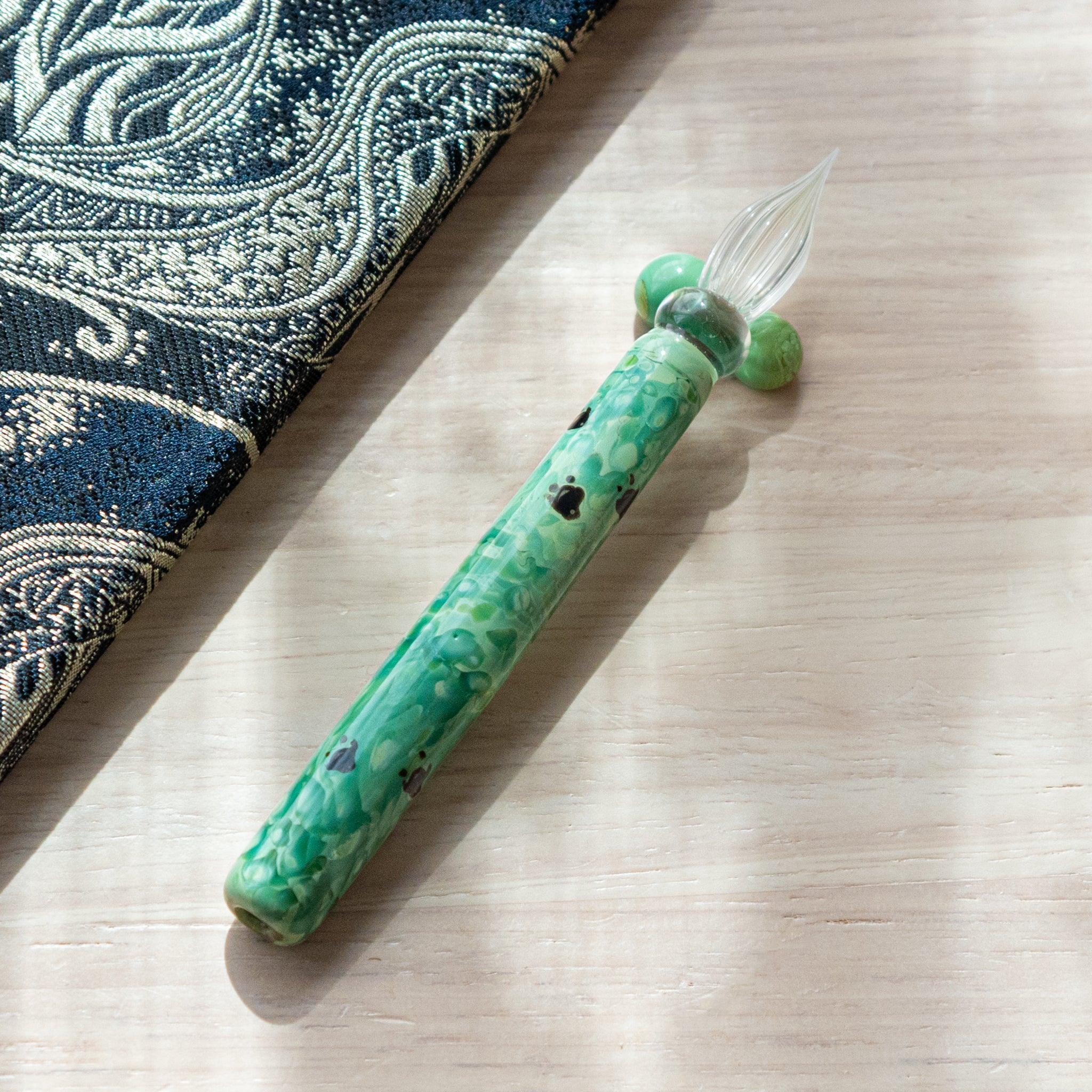 Emerald green glass pen with traditional Chidori design, showing birds over waves. Includes matching pen rest on wood and Nishijin textile notebook.