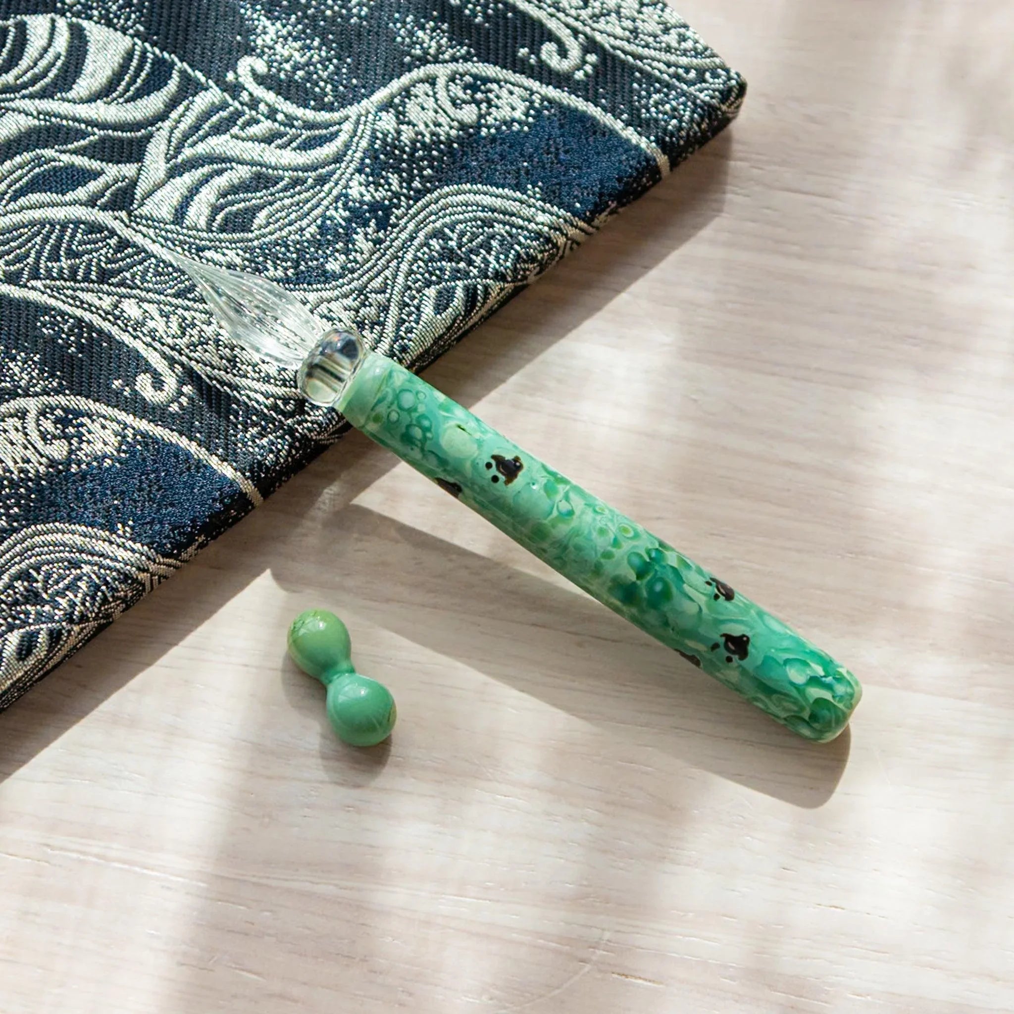 Flatlay of emerald glass dip pen showing traditional chidori design against decorative patterned fabric backdrop