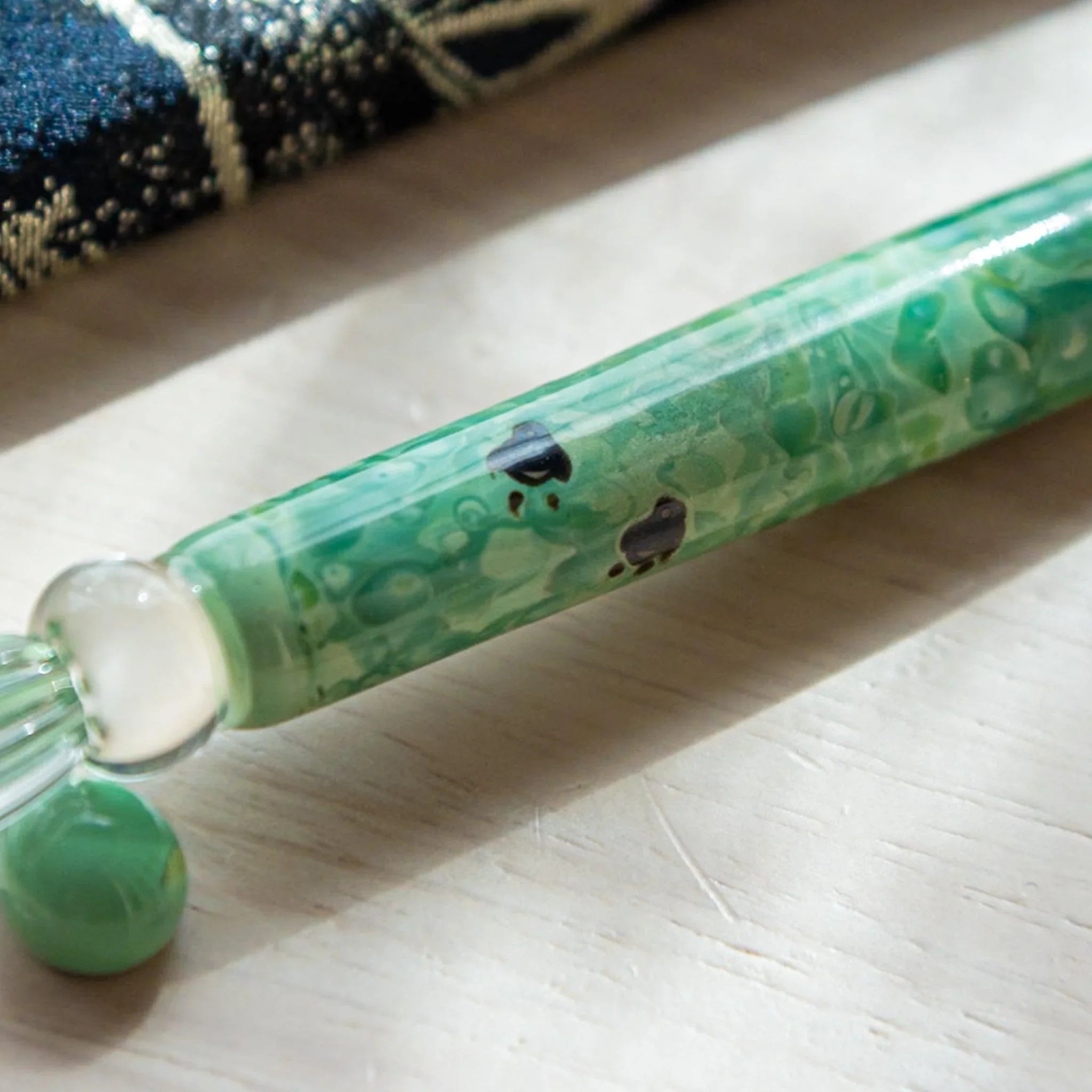 Product styling of emerald green glass dip pen with chidori motif positioned on neutral surface background shown