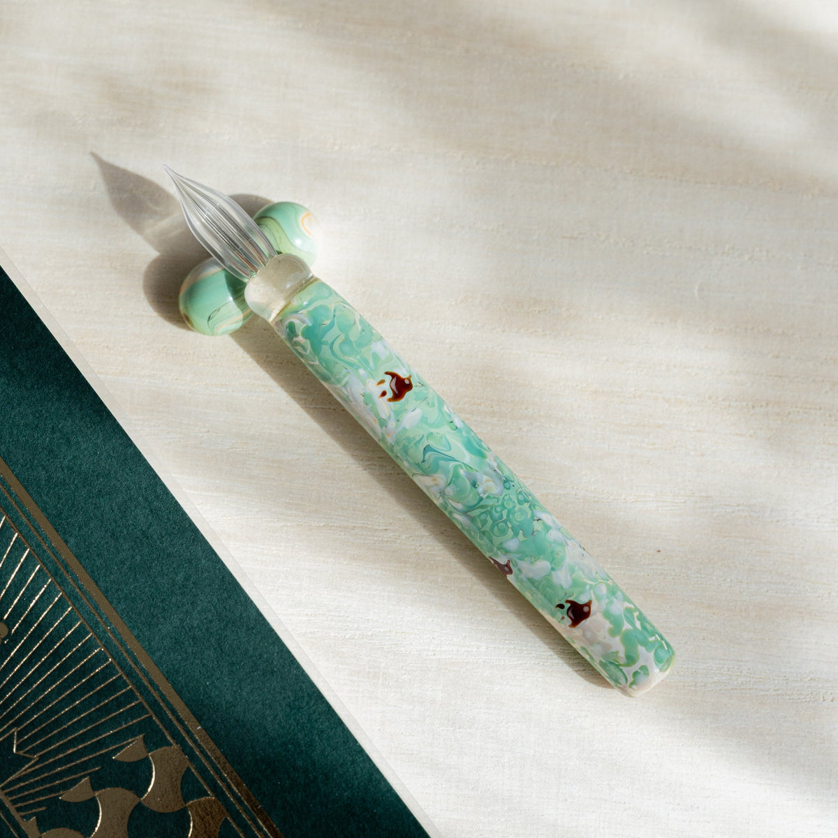 Chidori Mint Marble glass dip pen angled on pale wood with a green glass sphere pen rest at the nib