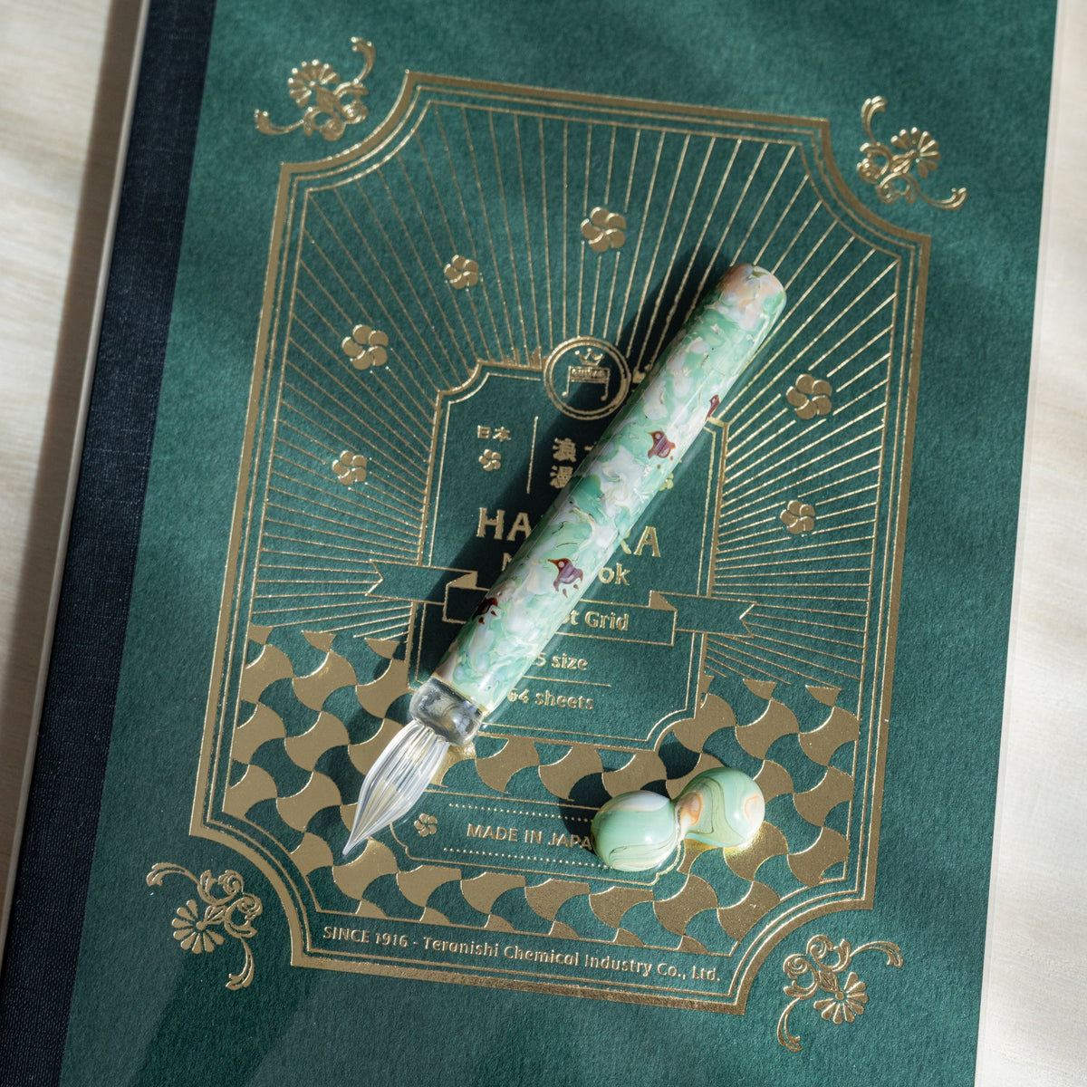 Chidori Mint Marble glass dip pen and pen rest on a green HAIKARA notebook cover with gold foil