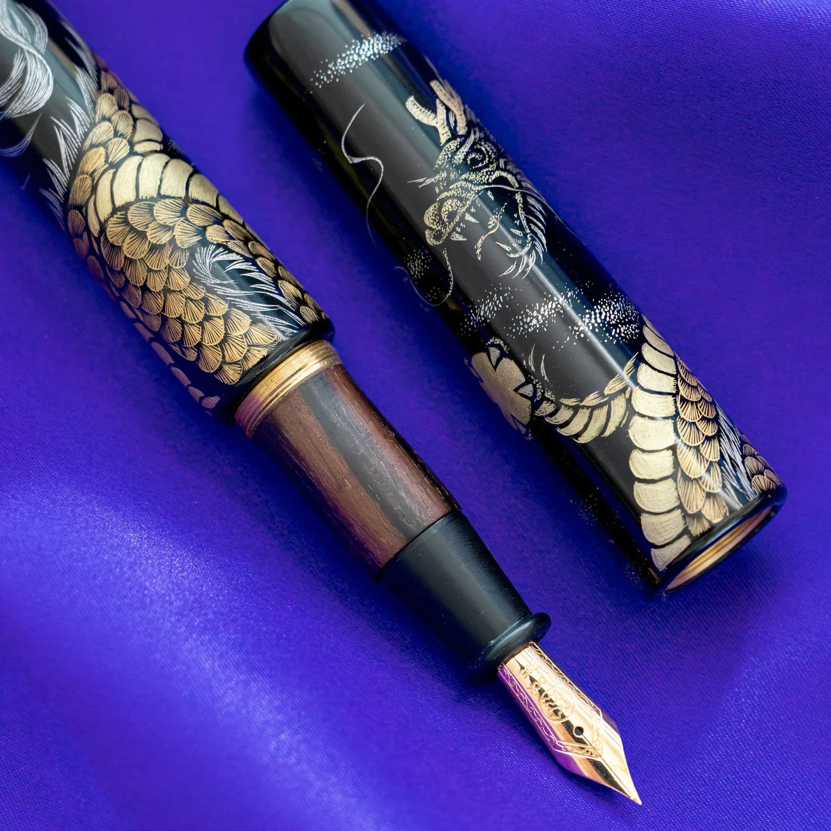Close-up of Chinkin Dragon fountain pen striped ebony grip and engraved 14K 585 gold nib beside the black lacquer cap