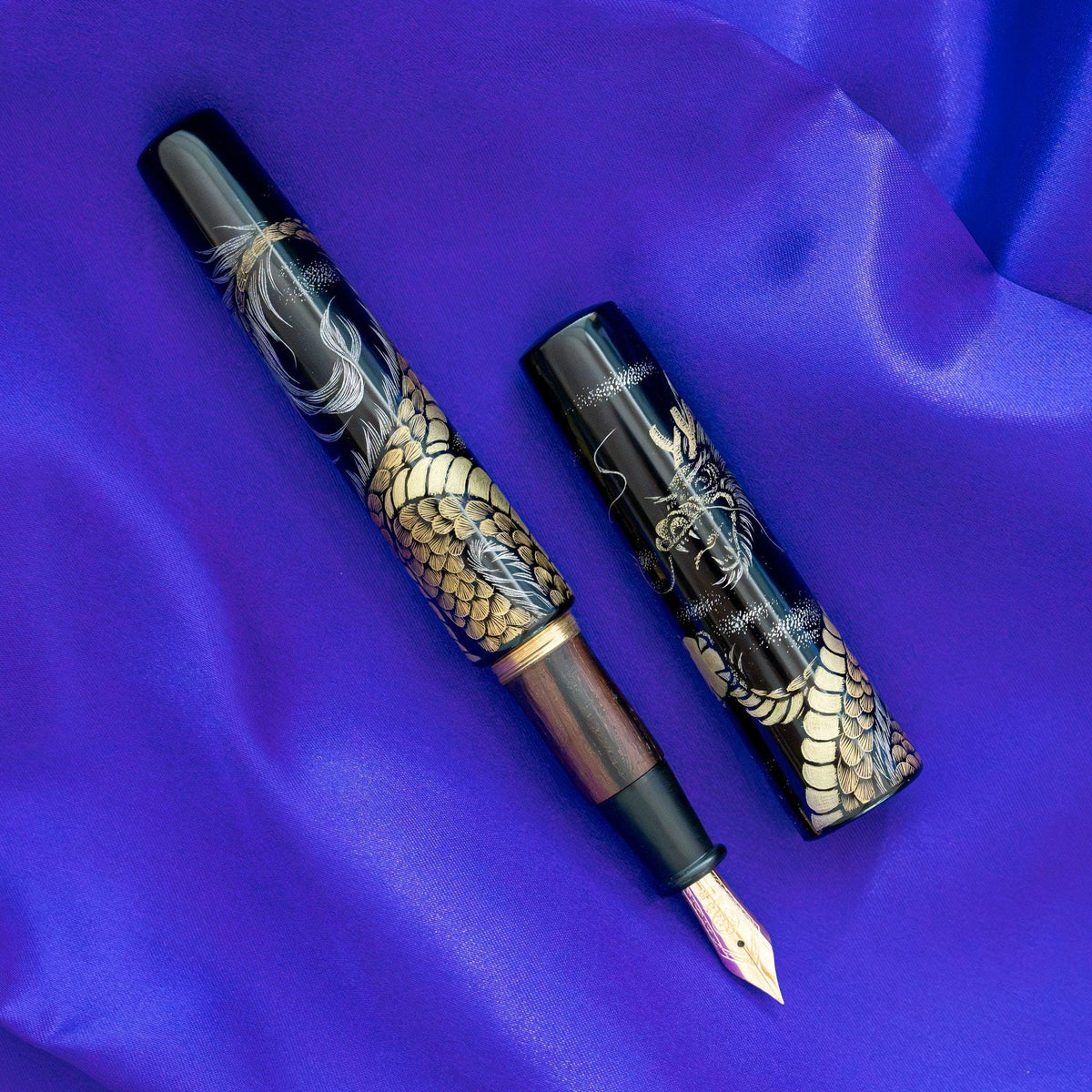 Chinkin Dragon Echizen lacquered fountain pen uncapped on purple satin, striped ebony grip, gold nib, dragon cap beside