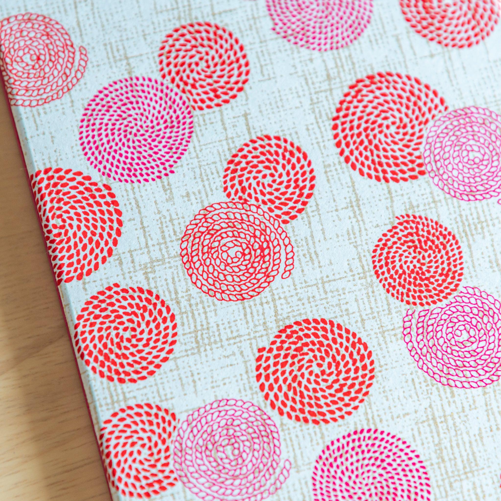 Close-up of washi-covered Goshuinsho stamp book with red and pink swirl floral patterns, perfect Japanese stationery.