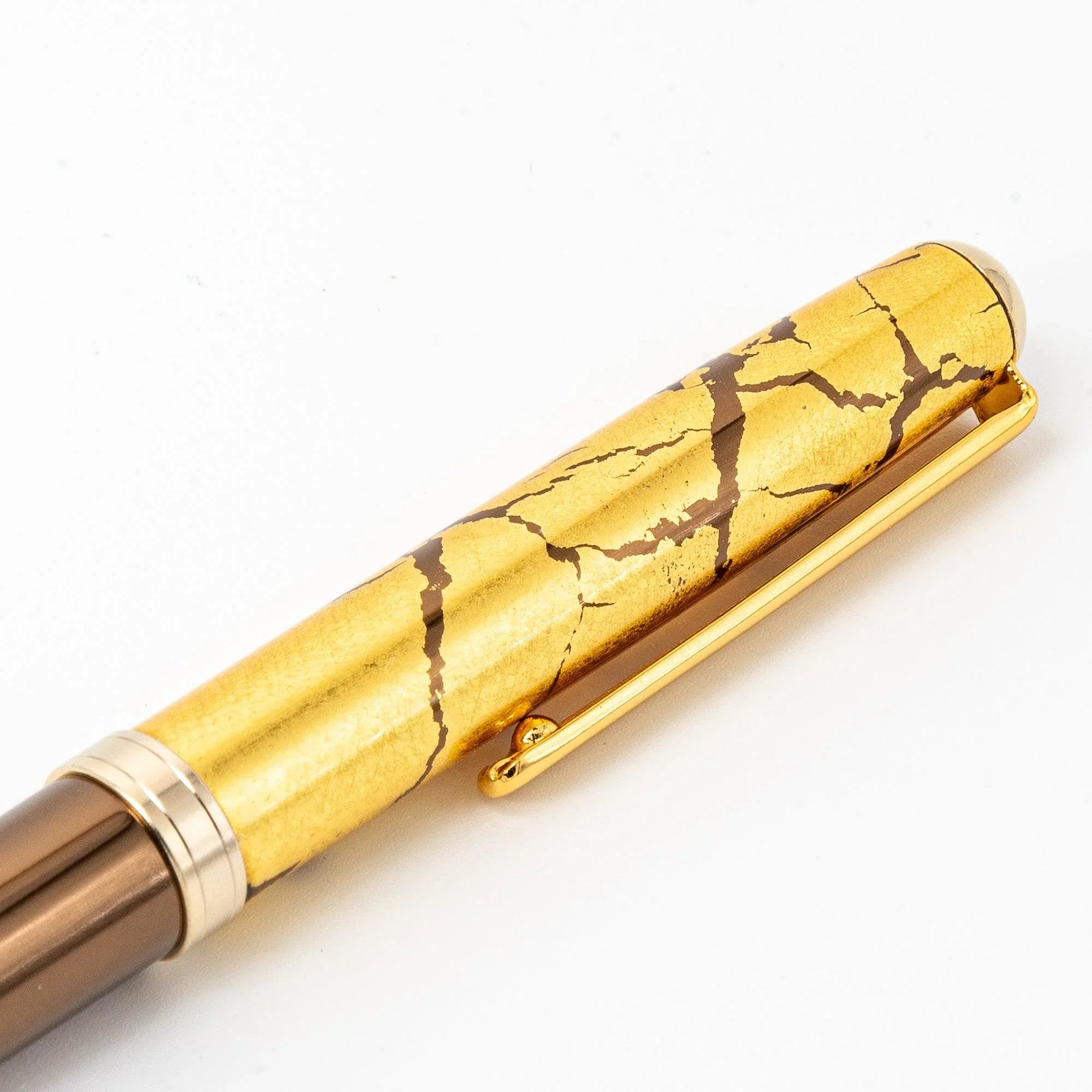 Close-up detail of Japanese brown ballpoint pen barrel with gold crackle cap texture on white background