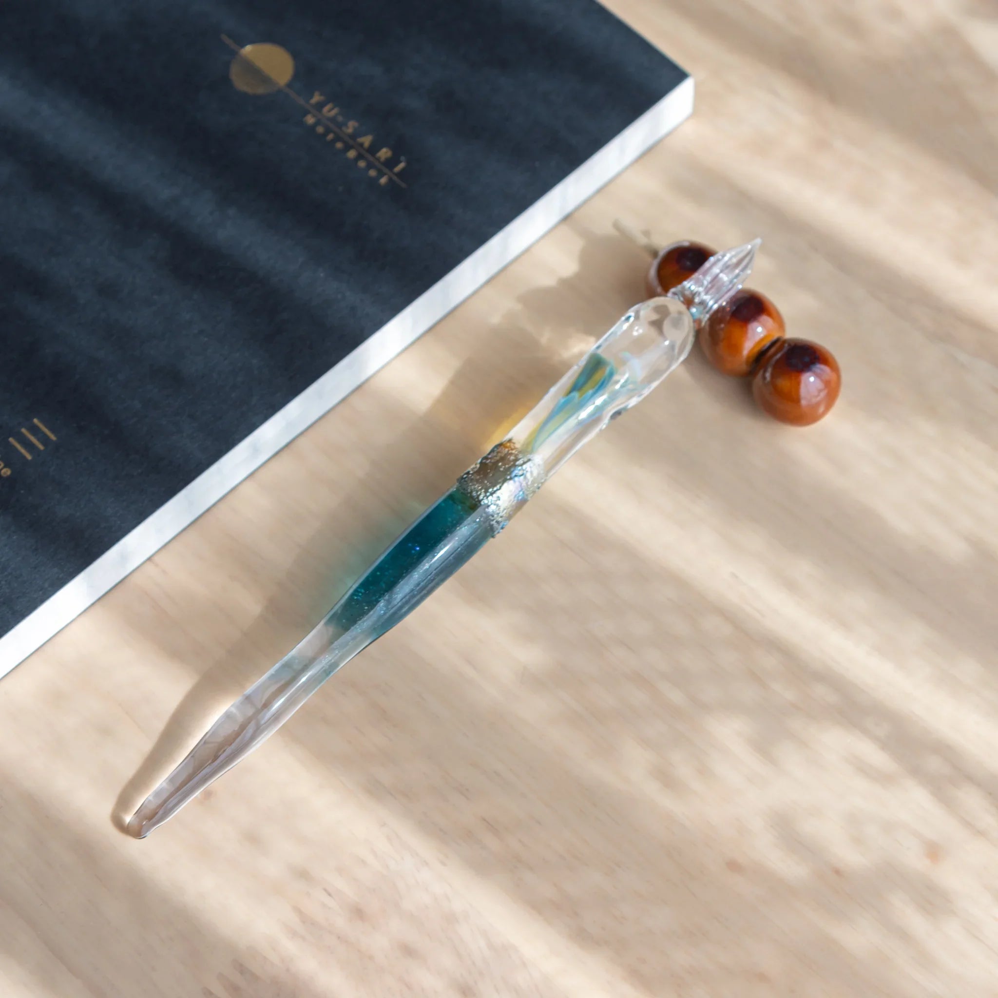 Dark burgundy dango pen rest with three round polished beads stacked vertically on translucent glass stick structure