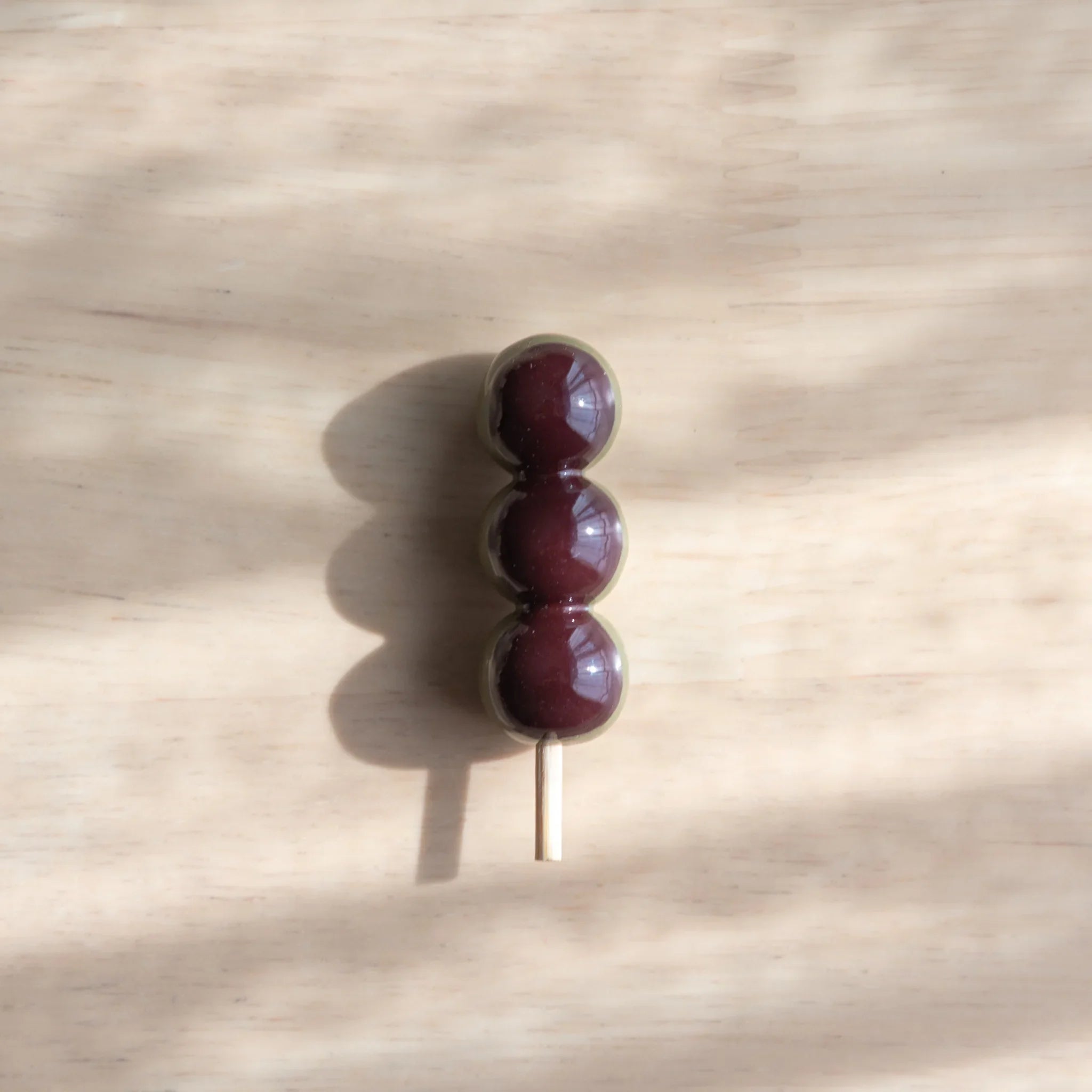 Deep burgundy and white dango pen rest with three stacked glossy spheres and decorative wooden dowel base detail