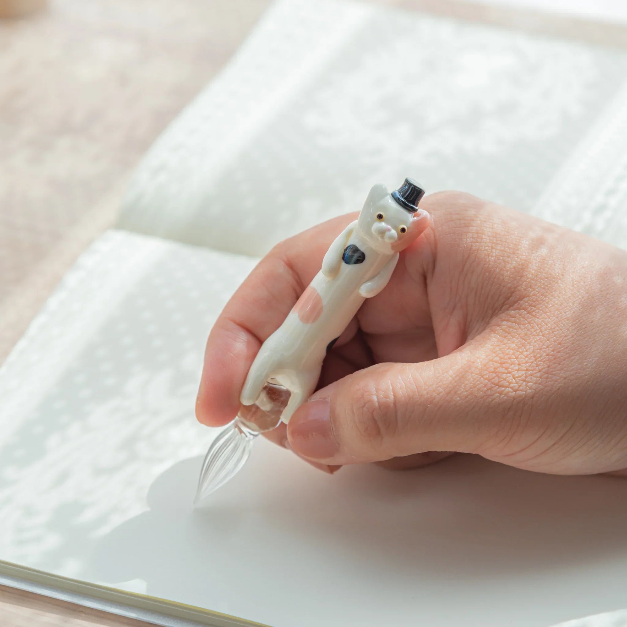 Whimsical spotted cat glass dip pen featuring tabby design clutching hand-blown glass ink barrel well