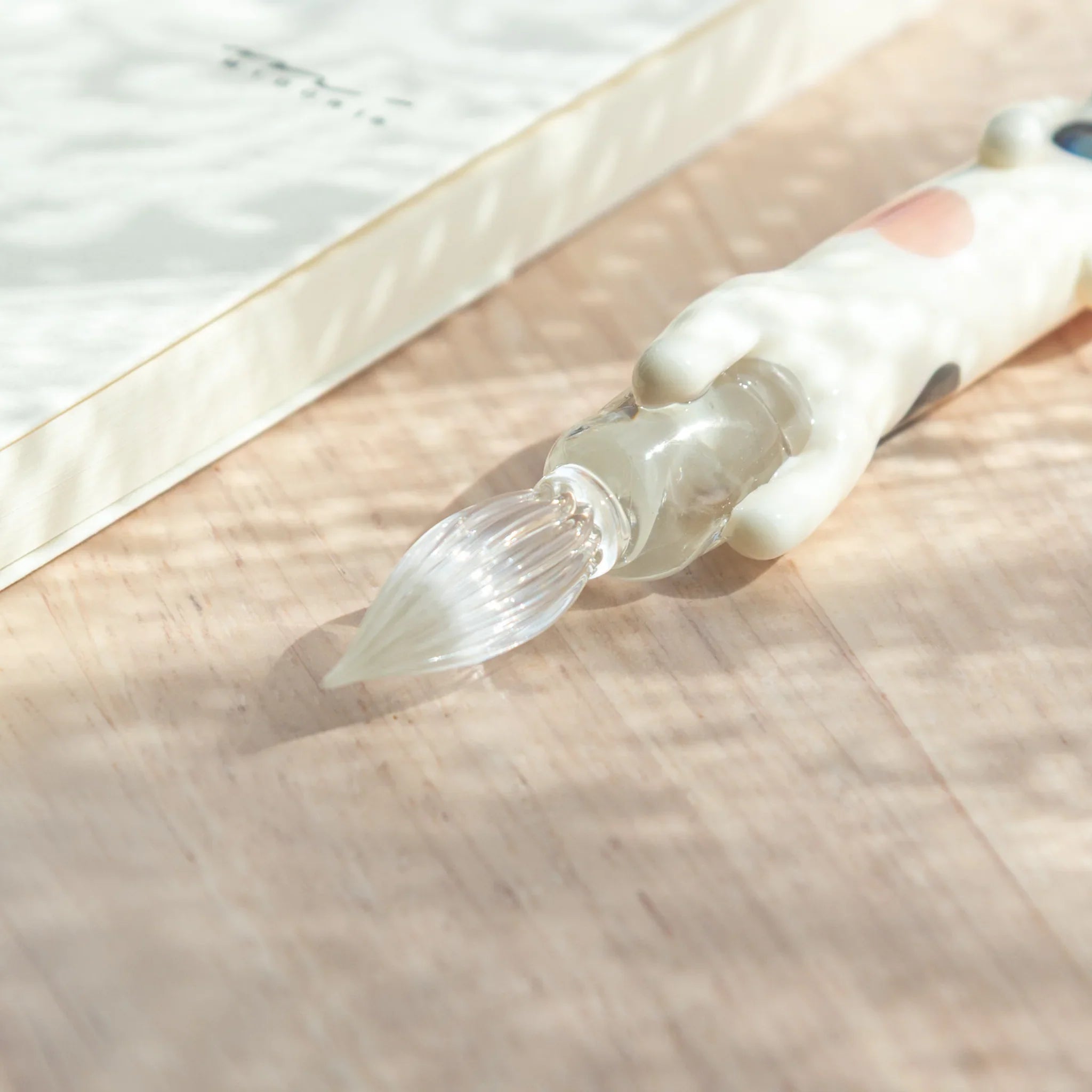 Decorative cat glass dip pen featuring dapper spotted kitten perched on textured sand base holder with unique design