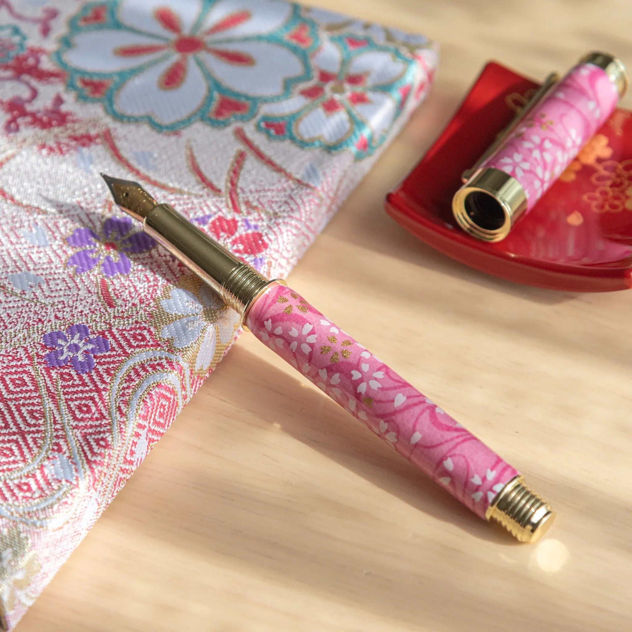 Pink Mino washi Japanese fountain pen uncapped showing gold nib, resting on a multicolor woven floral textile lie