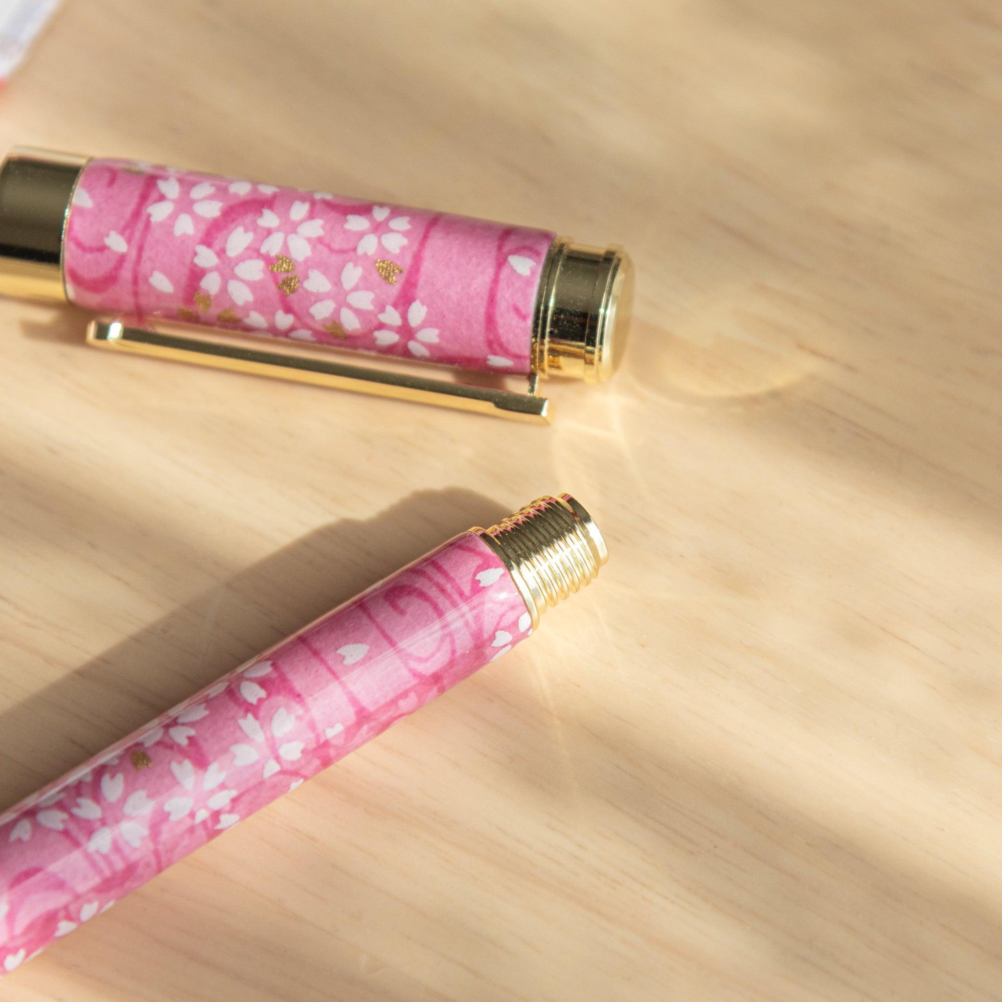 Close-up of pink sakura-patterned fountain pen cap and body with gold details placed on light wooden surface.