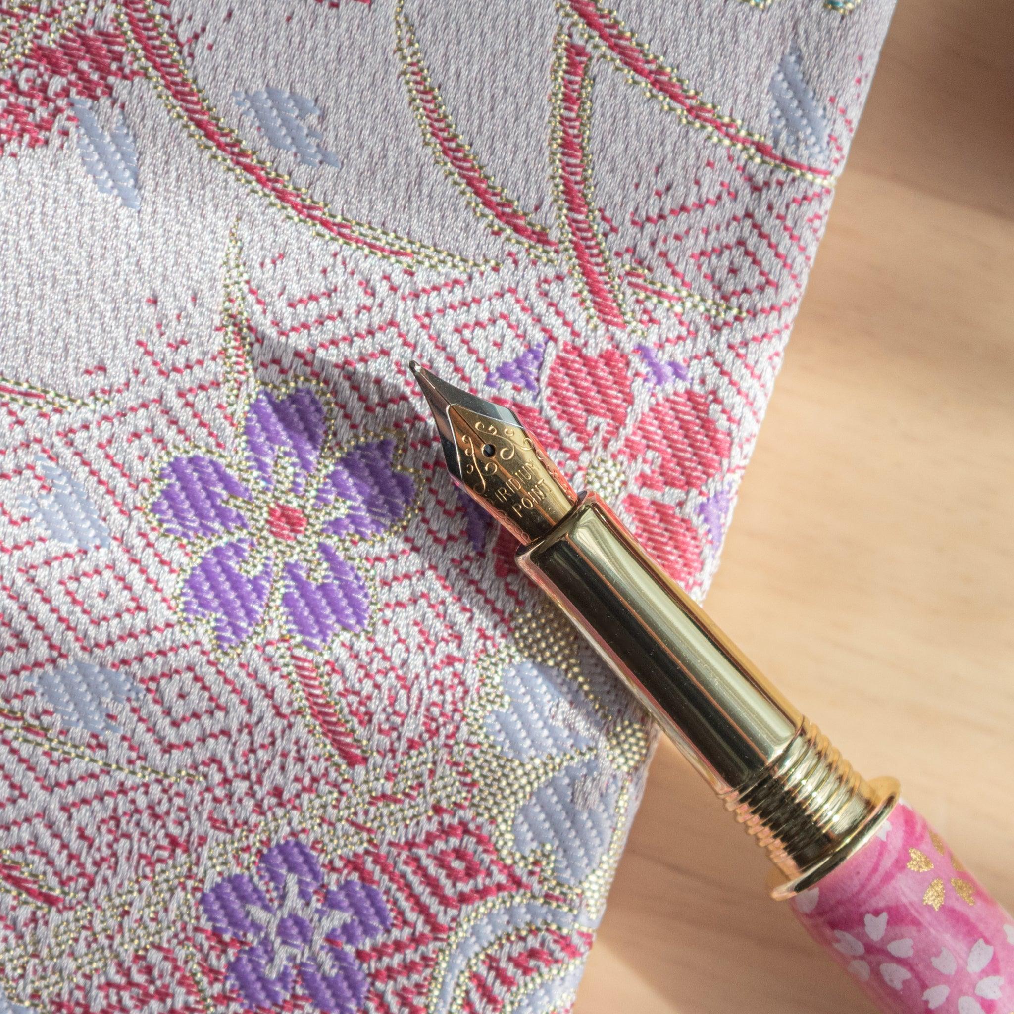 Gold-nibbed pink sakura-themed fountain pen on floral-patterned fabric in soft light.
