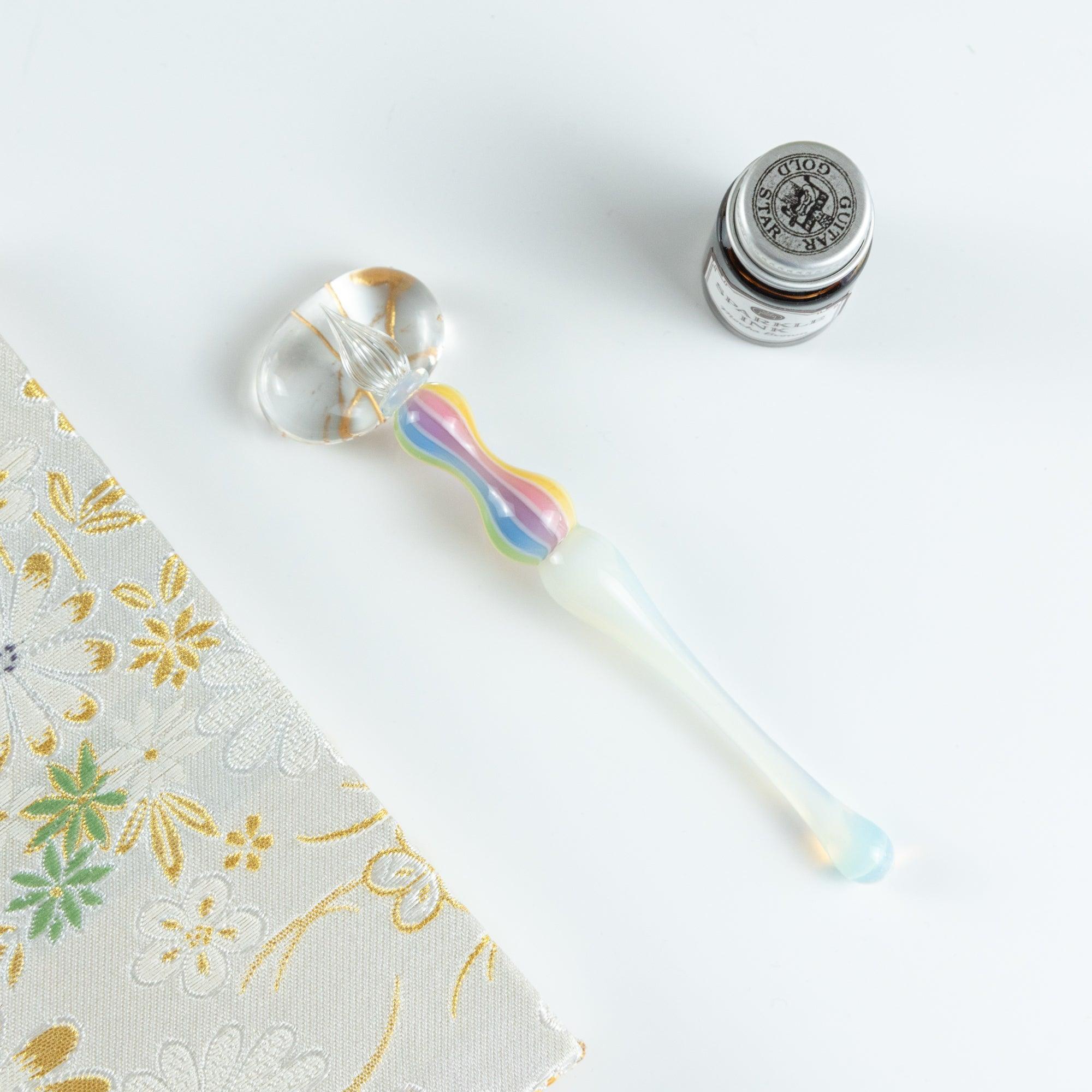 Glass pen with rainbow-colored handle placed on a white desk. Great for Japanese stationery lovers.