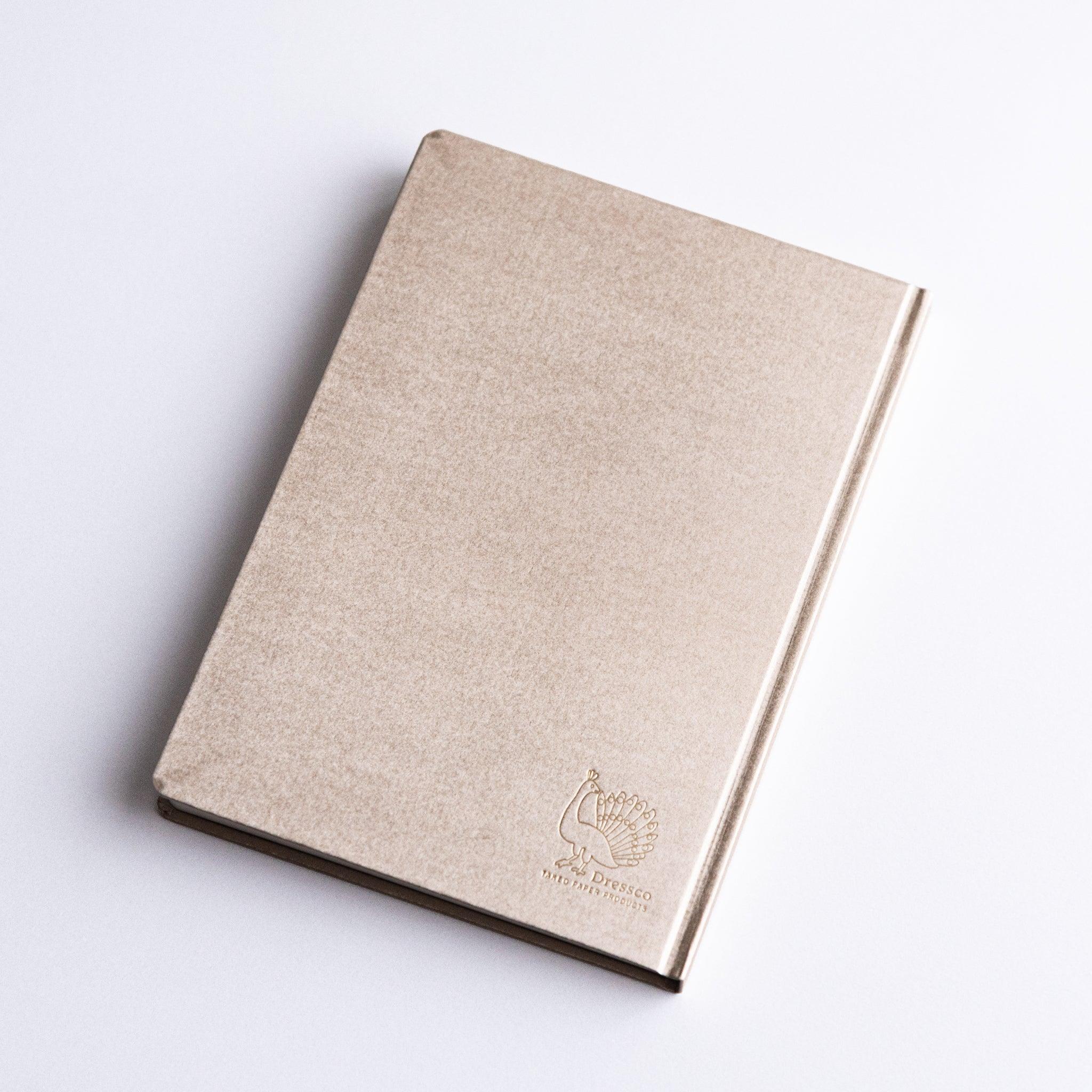 Angled view of Dressco Bank Ledger Paper Japanese Notebook in Champagne Gold with embossed logo.