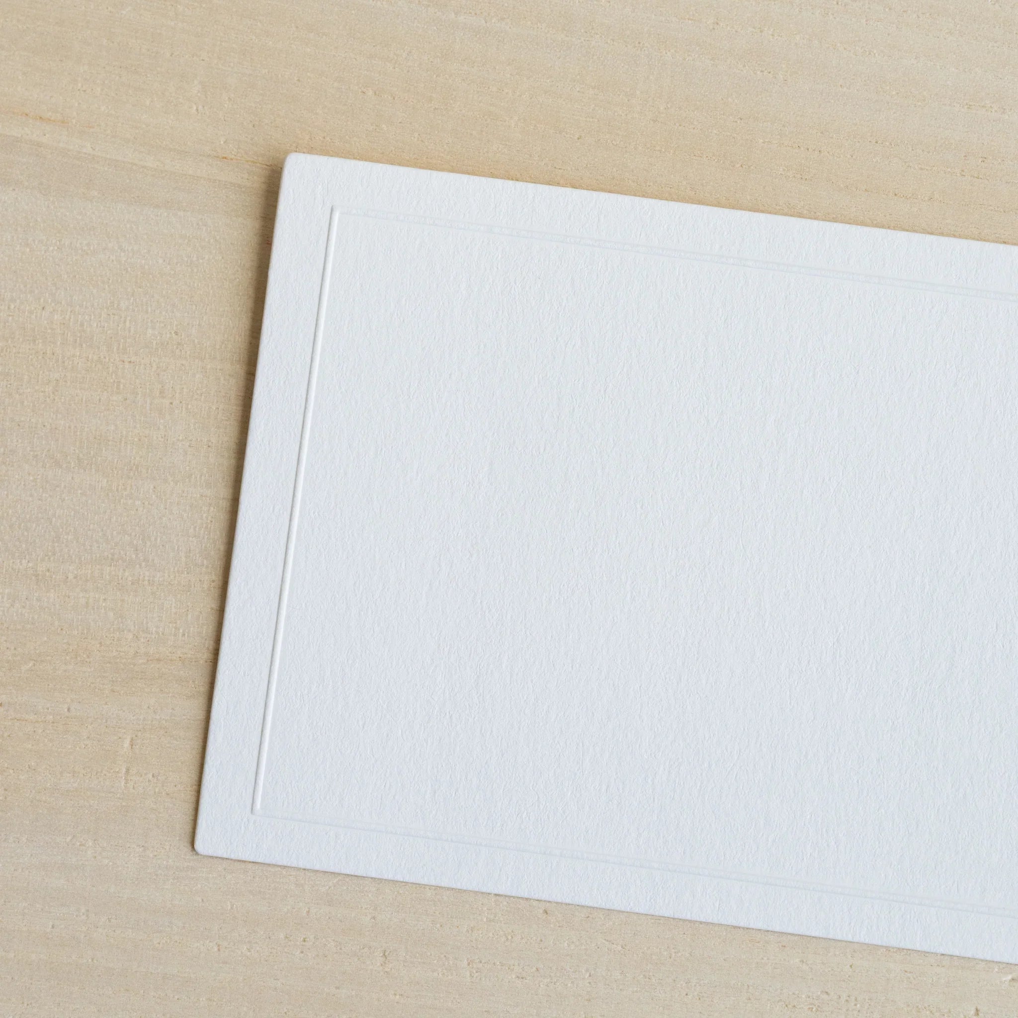 Single Conqueror laid paper message card with embossed rectangular border frame, shown at an angle on light wood surface