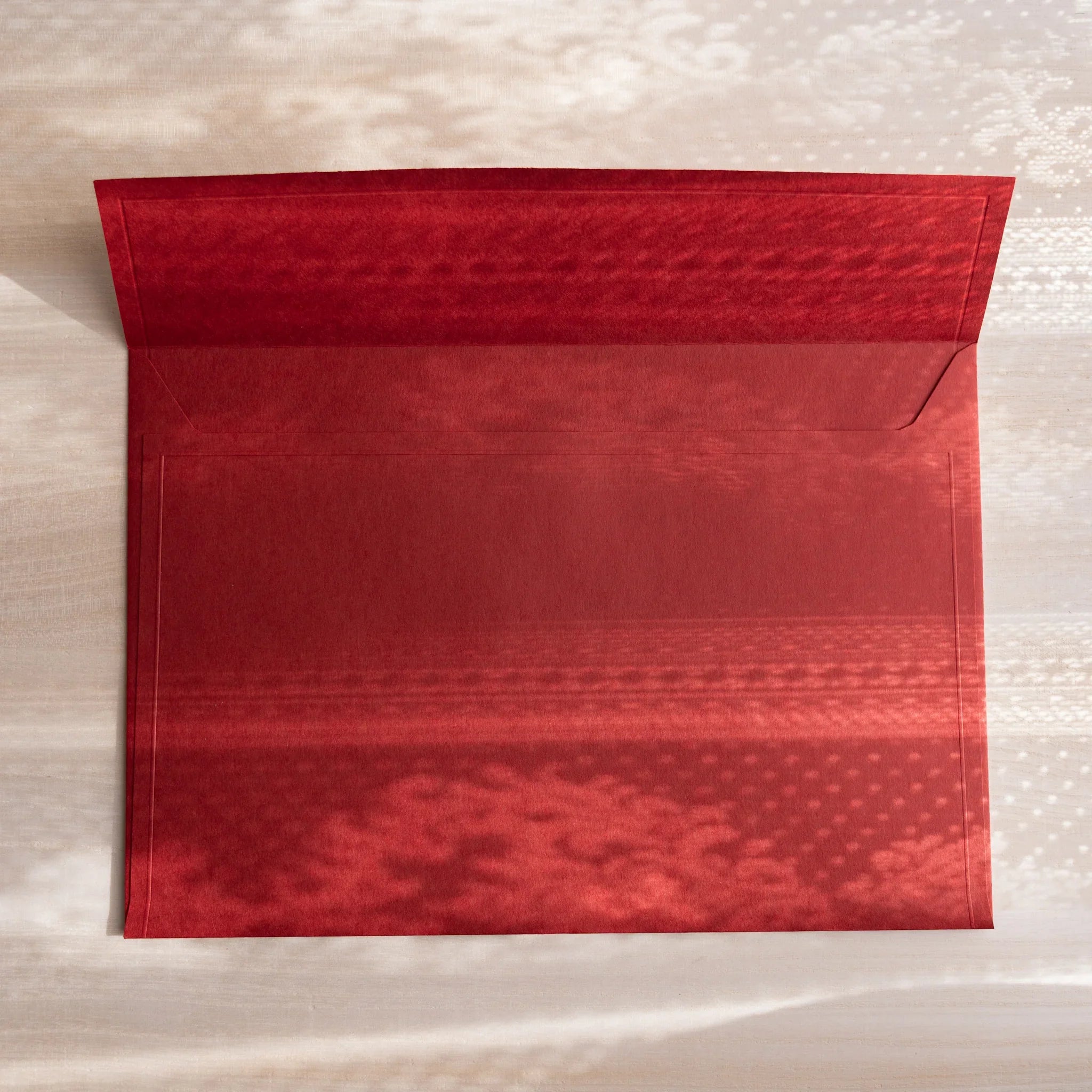 Large red embossed envelope with open flap, showing textured pattern on deep crimson paper