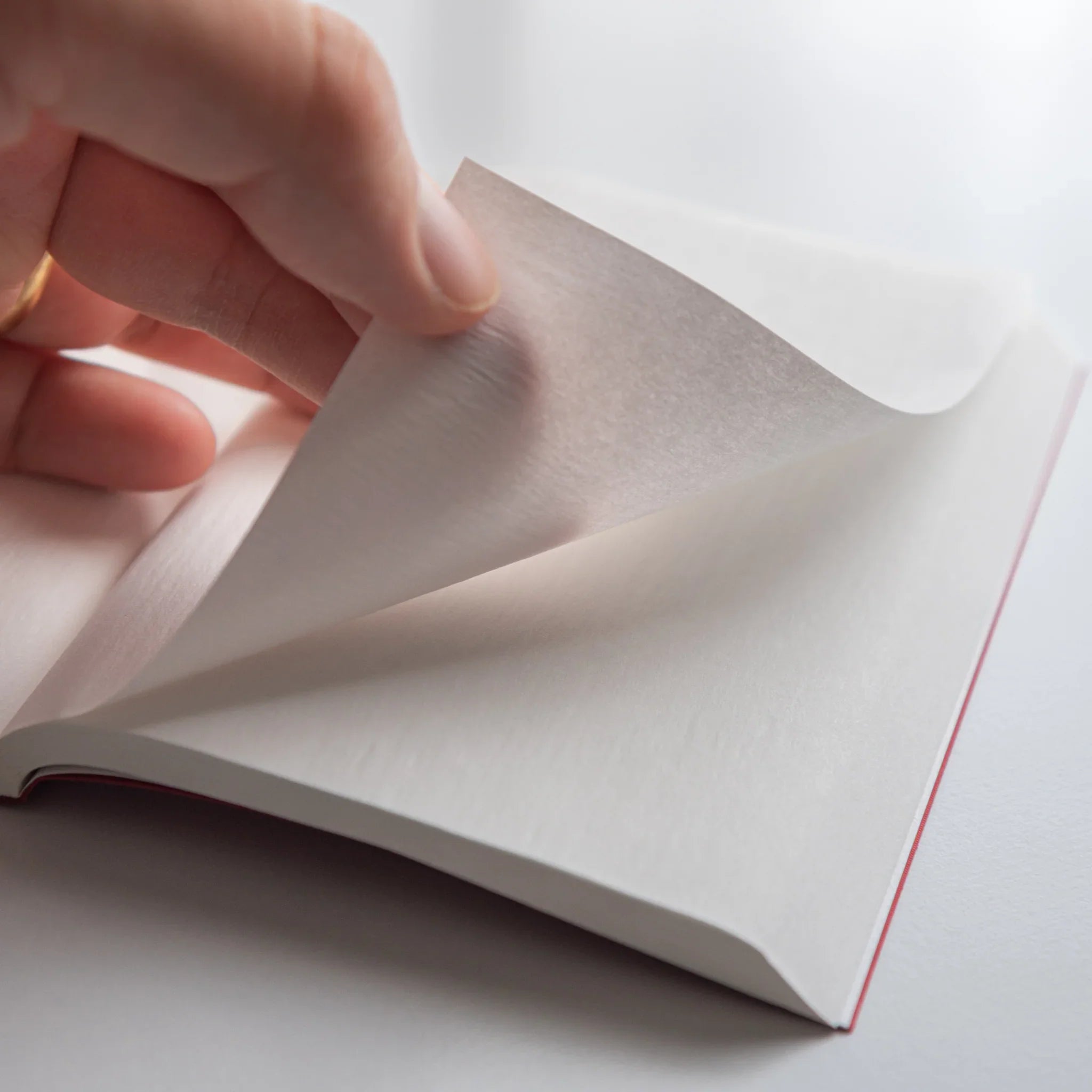 Hand turning thin, translucent onion-skin page of Dressco Pink Onion Skin Japanese Notebook A6.