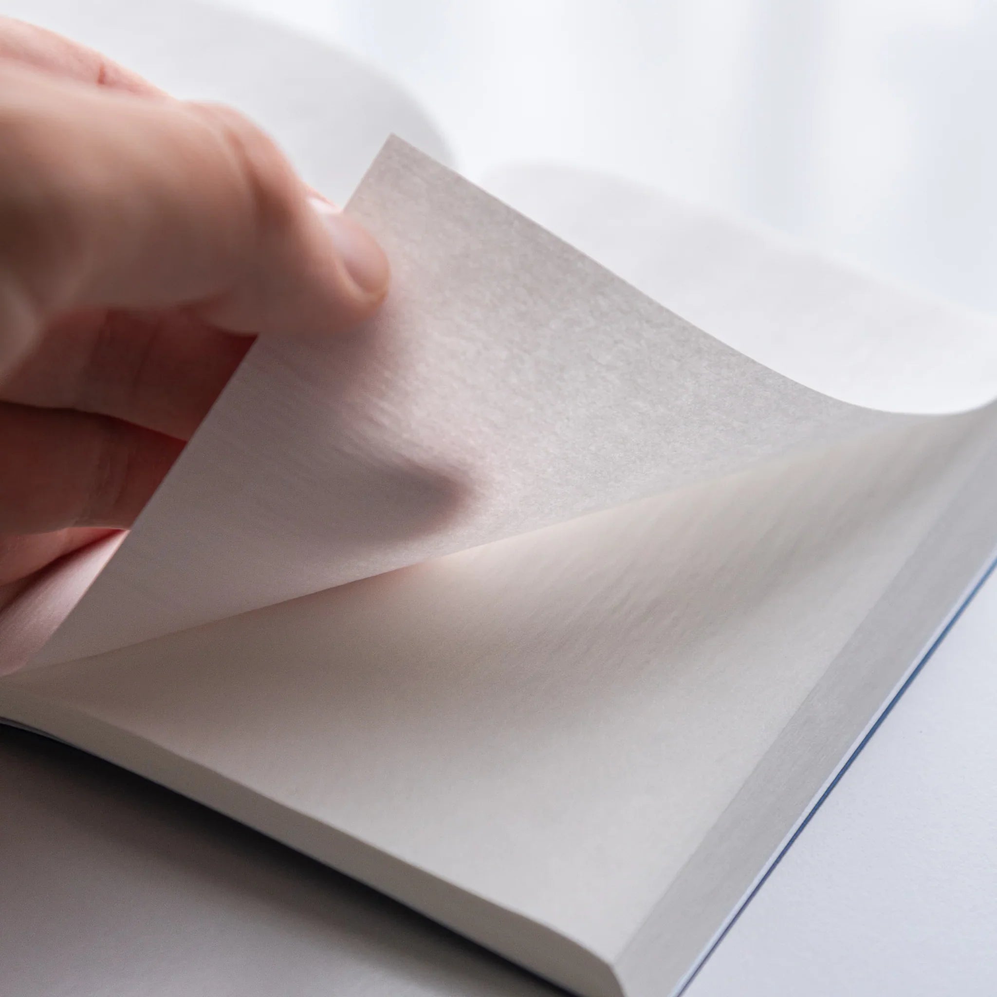 Hand flipping thin onion-skin page of Dressco Blue Onion Skin Japanese Notebook showing translucence.