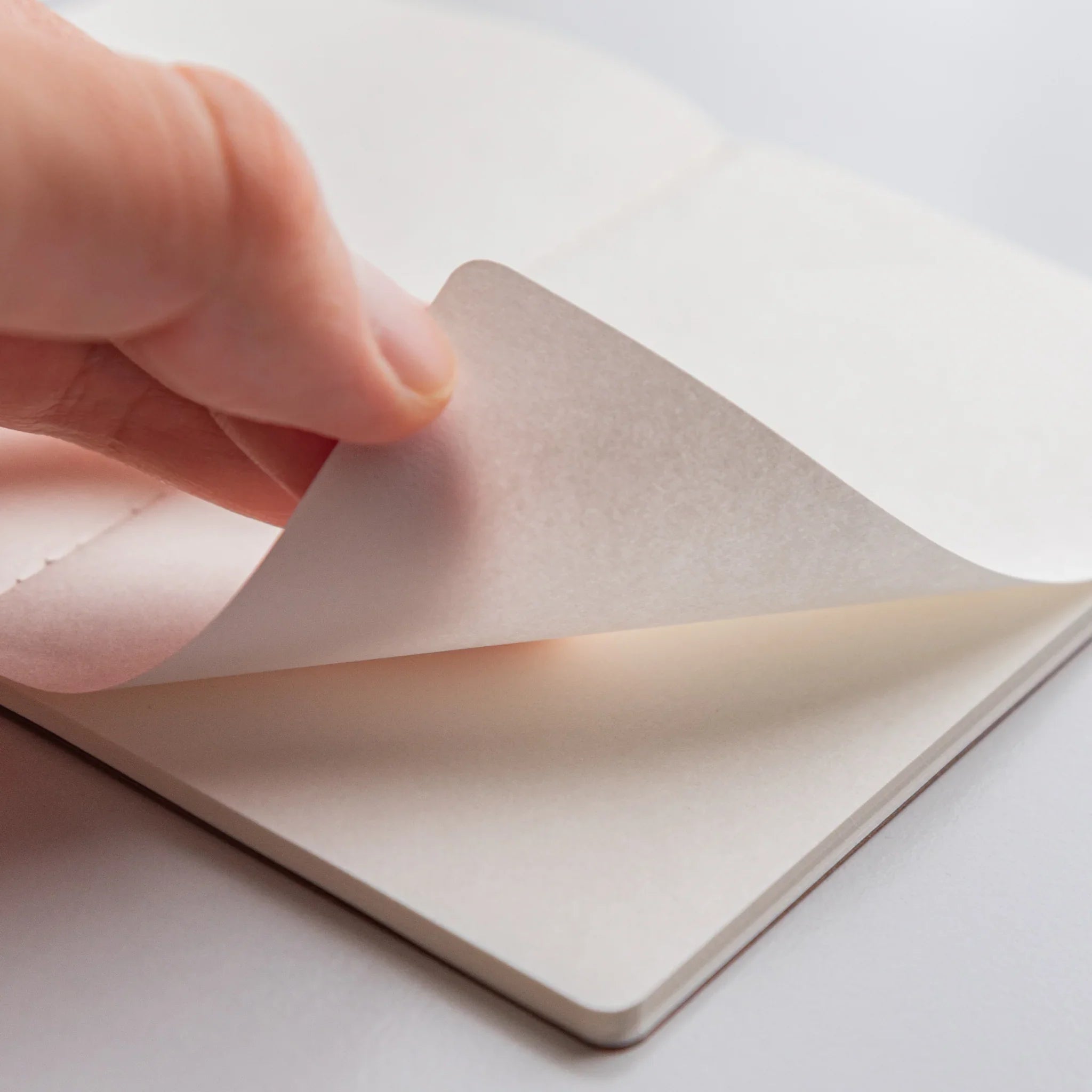 Hand flipping a page of a Japanese notebook made from Bank Ledger Paper to reveal blank sheets.