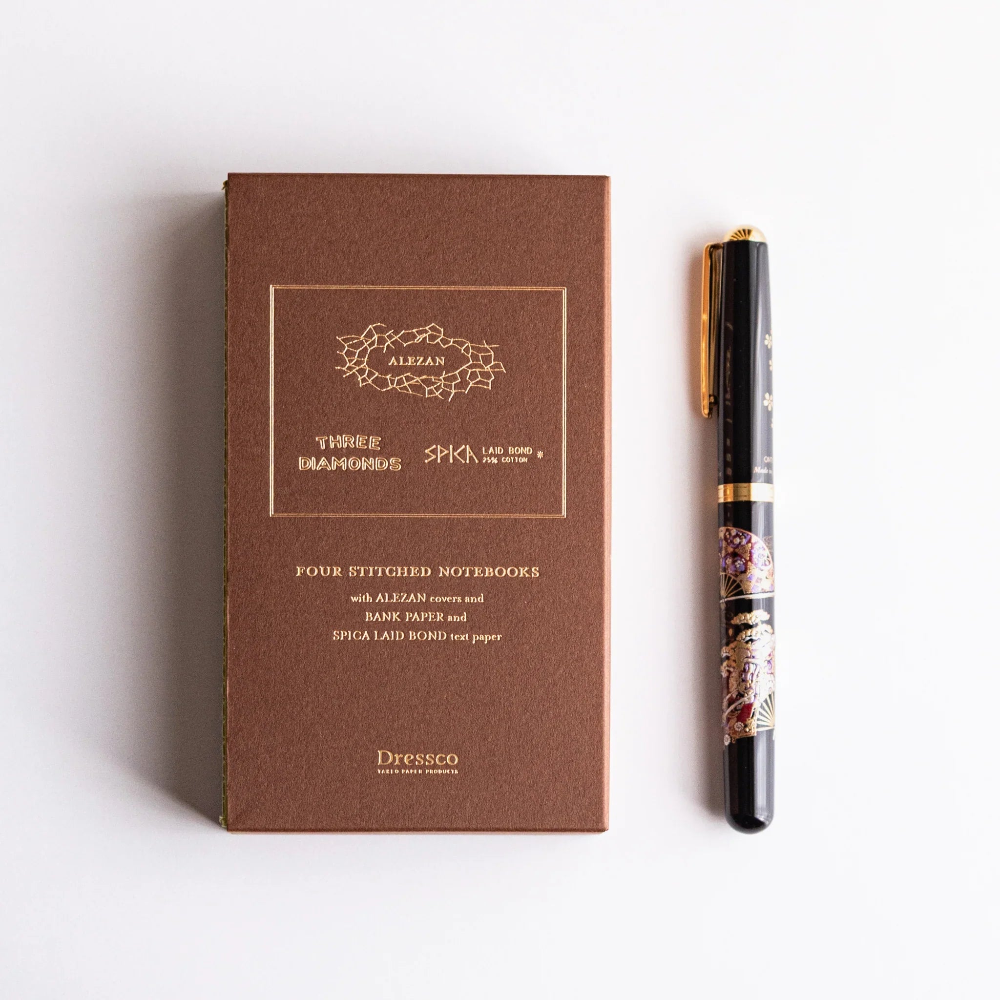 Dressco stitched Japanese notebook set in Alezan book case alongside an elegant pen, showcasing refined craftsmanship.