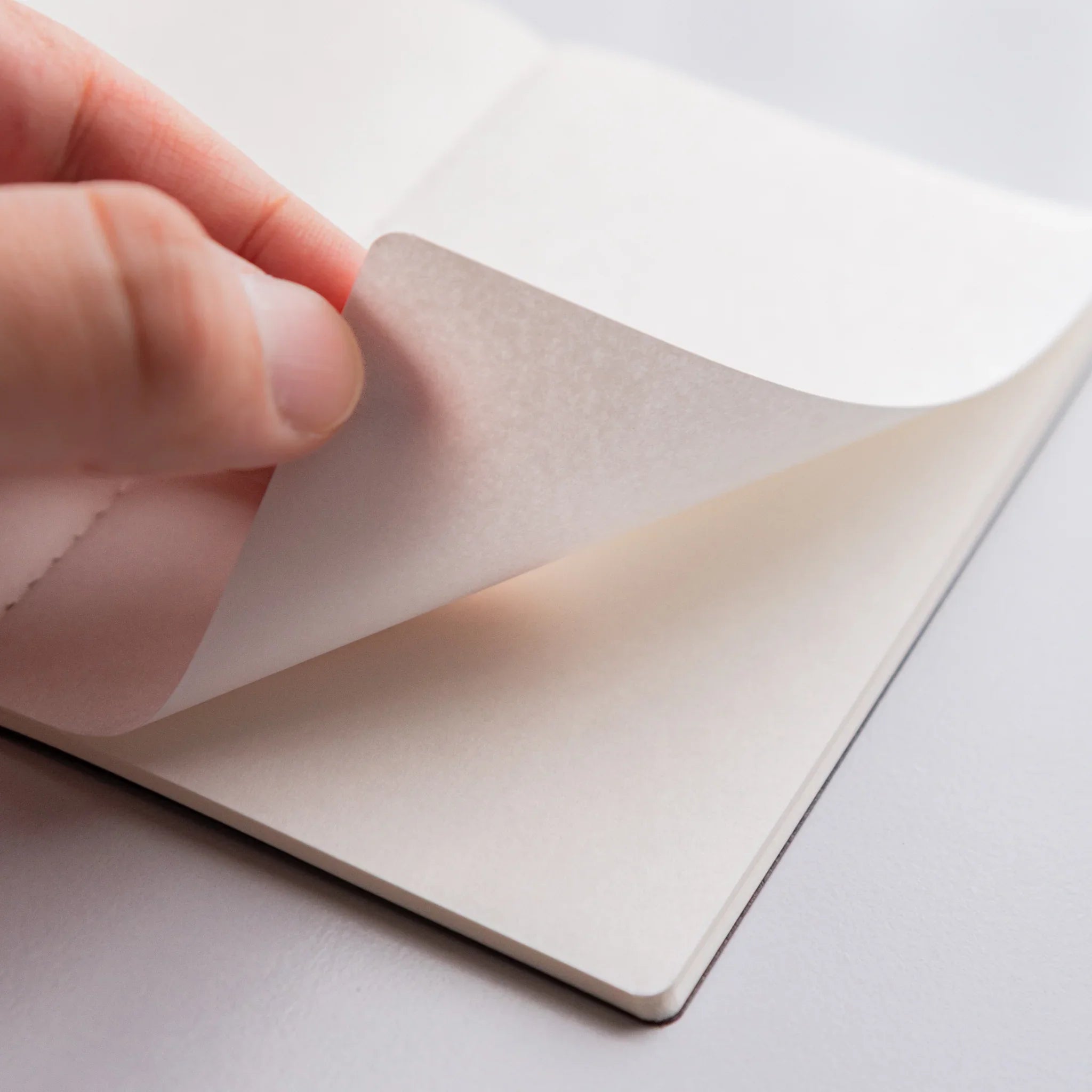 Hand turning a delicate page of Bank Ledger Paper Japanese notebook, highlighting tactile paper quality and craftsmanship.