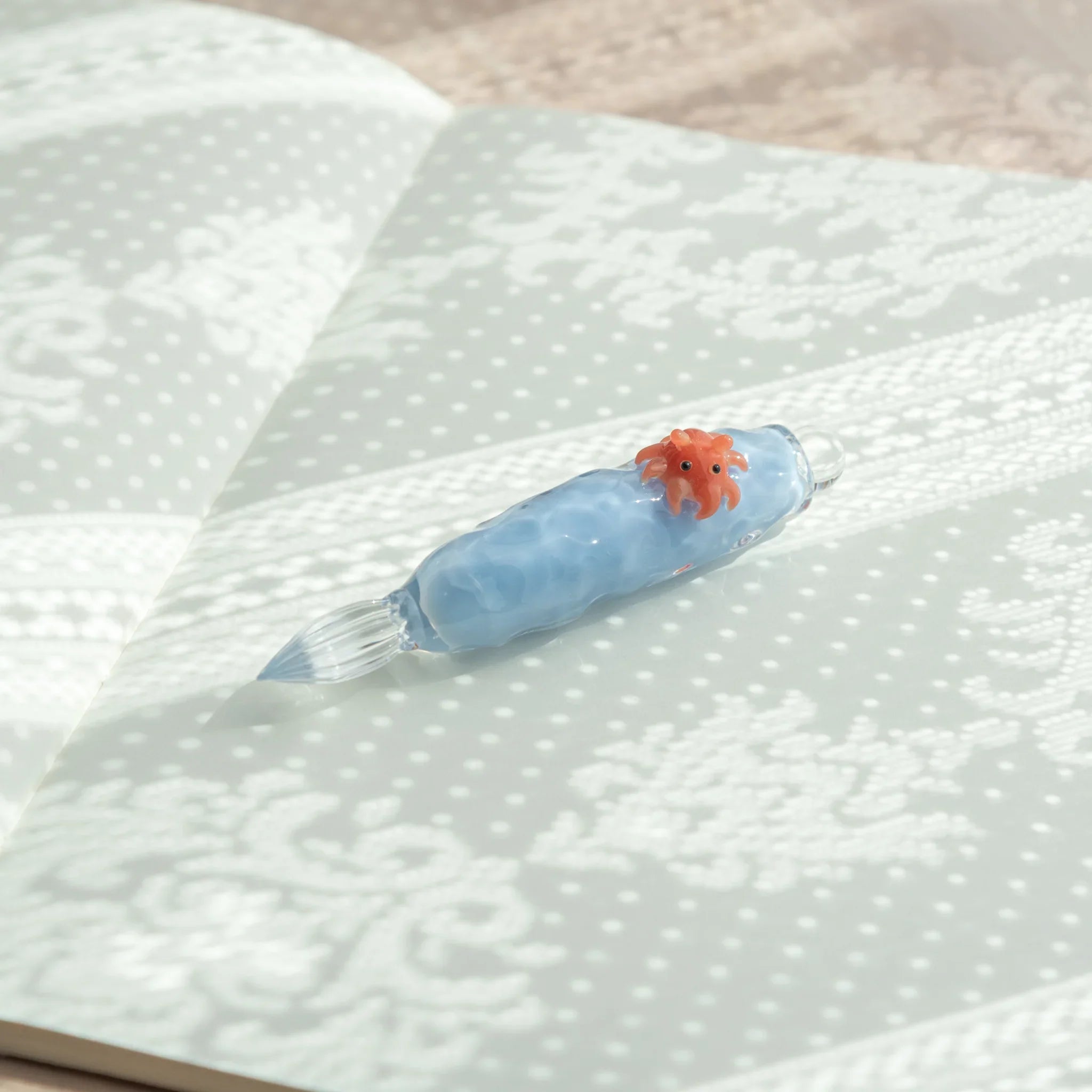 Unique glass dip pen featuring dumbo octopus sculpture on glass bottle with sand-textured ceramic base