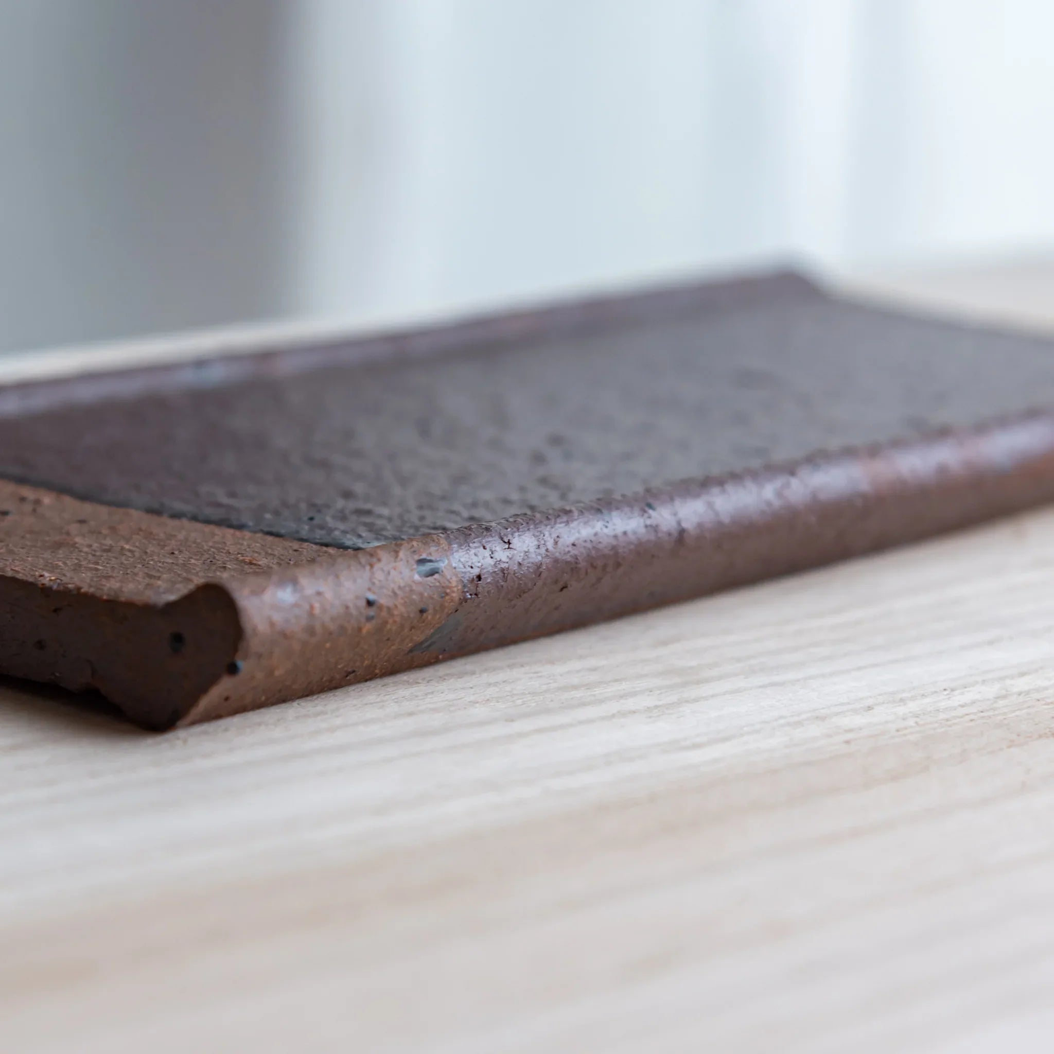 Japanese Pen Tray Desk Accessory side view of red ceramic tray showing thickness and brown edge on wooden surface.