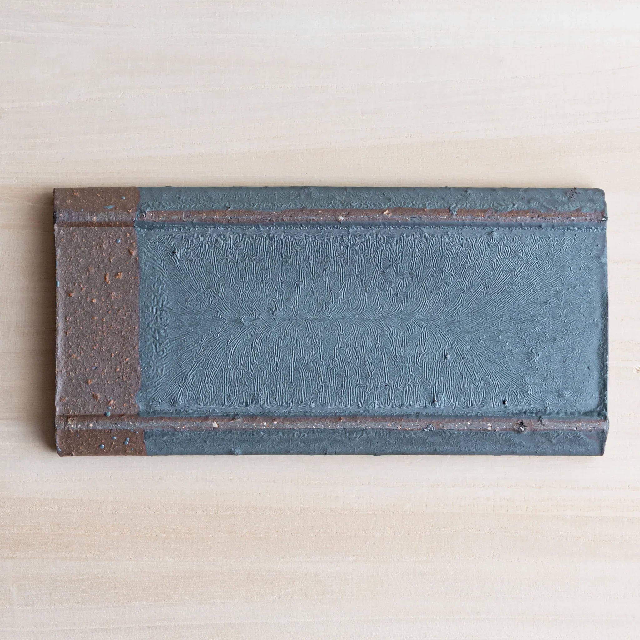Japanese Pen Tray Desk Accessory top view of silver gray ceramic tray with brown ends on light wooden surface.
