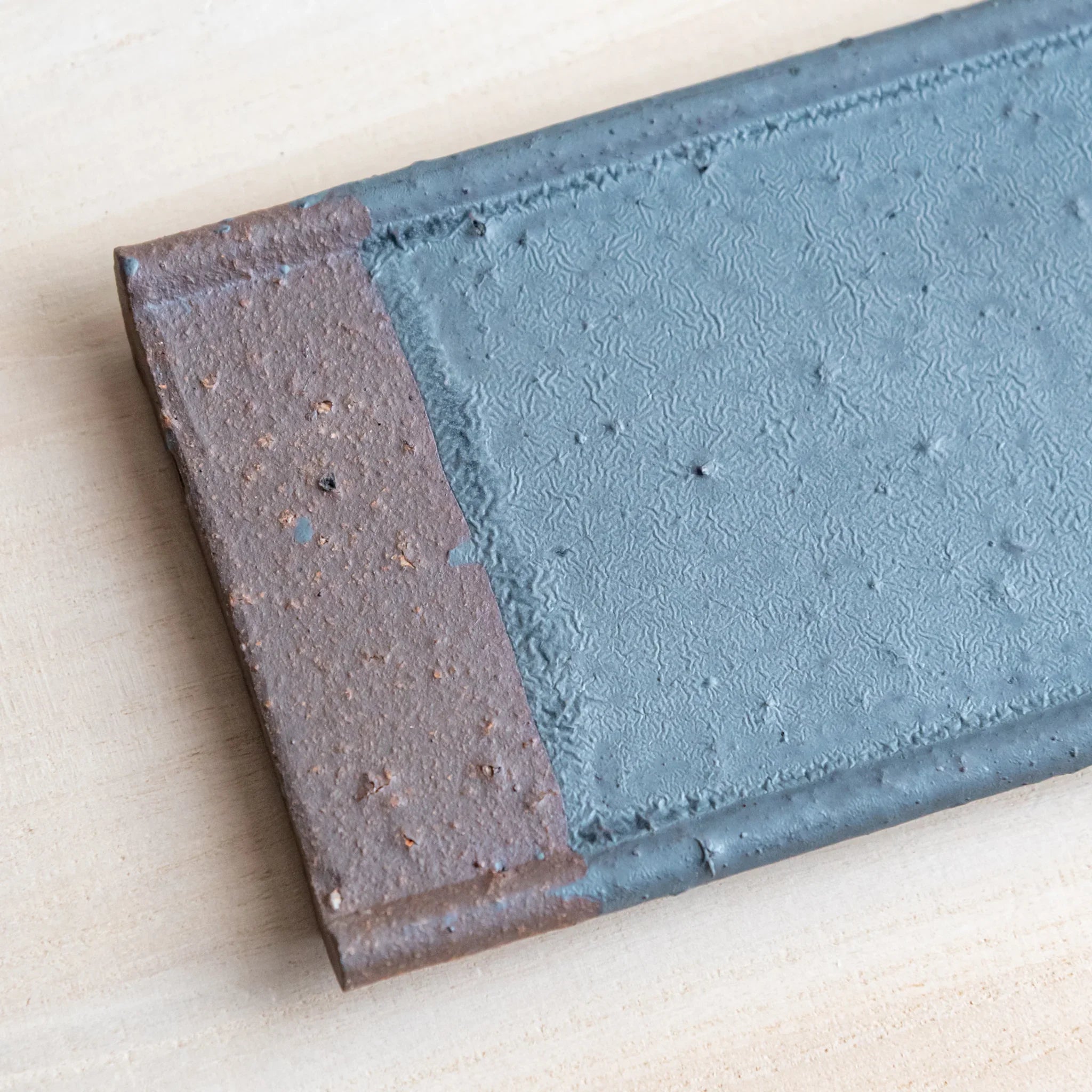 Japanese Pen Tray Desk Accessory close-up angled view of silver gray ceramic tray with brown end on wooden surface.