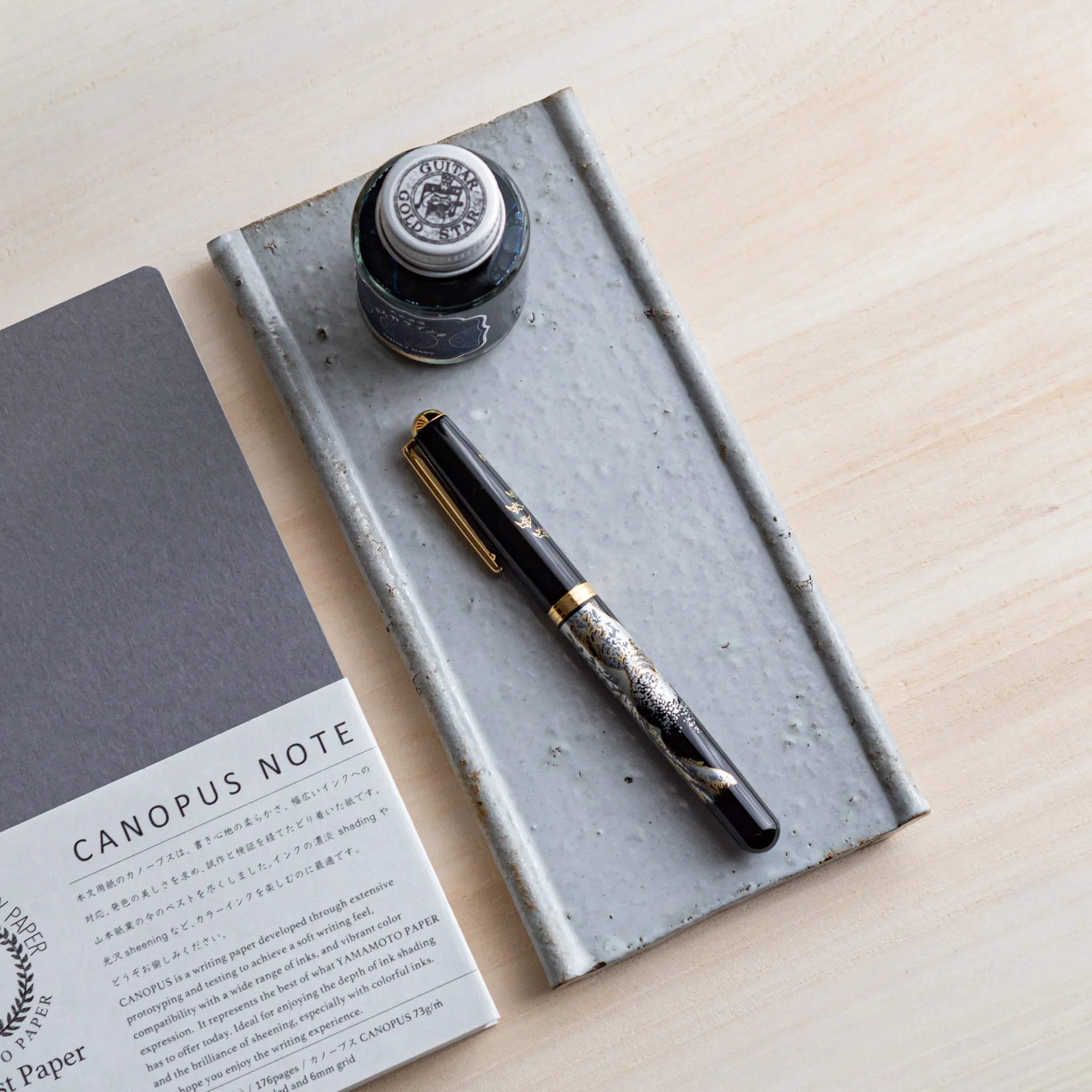 Japanese Pen Tray Desk Accessory with white glaze ceramic tray holding a fountain pen next to a notebook.