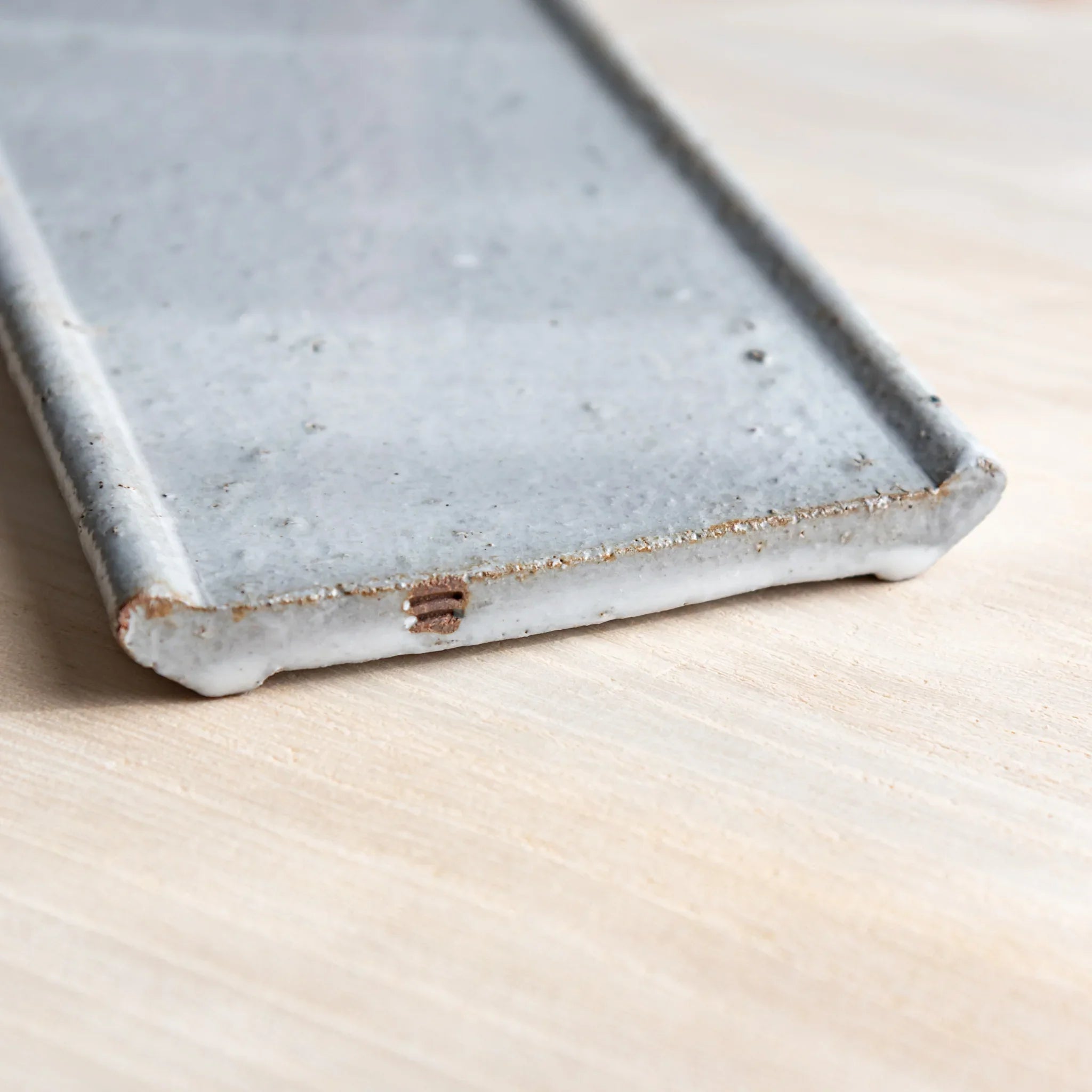 Japanese Pen Tray Desk Accessory showing close-up angled view of white glaze ceramic tray with on light wood desk.